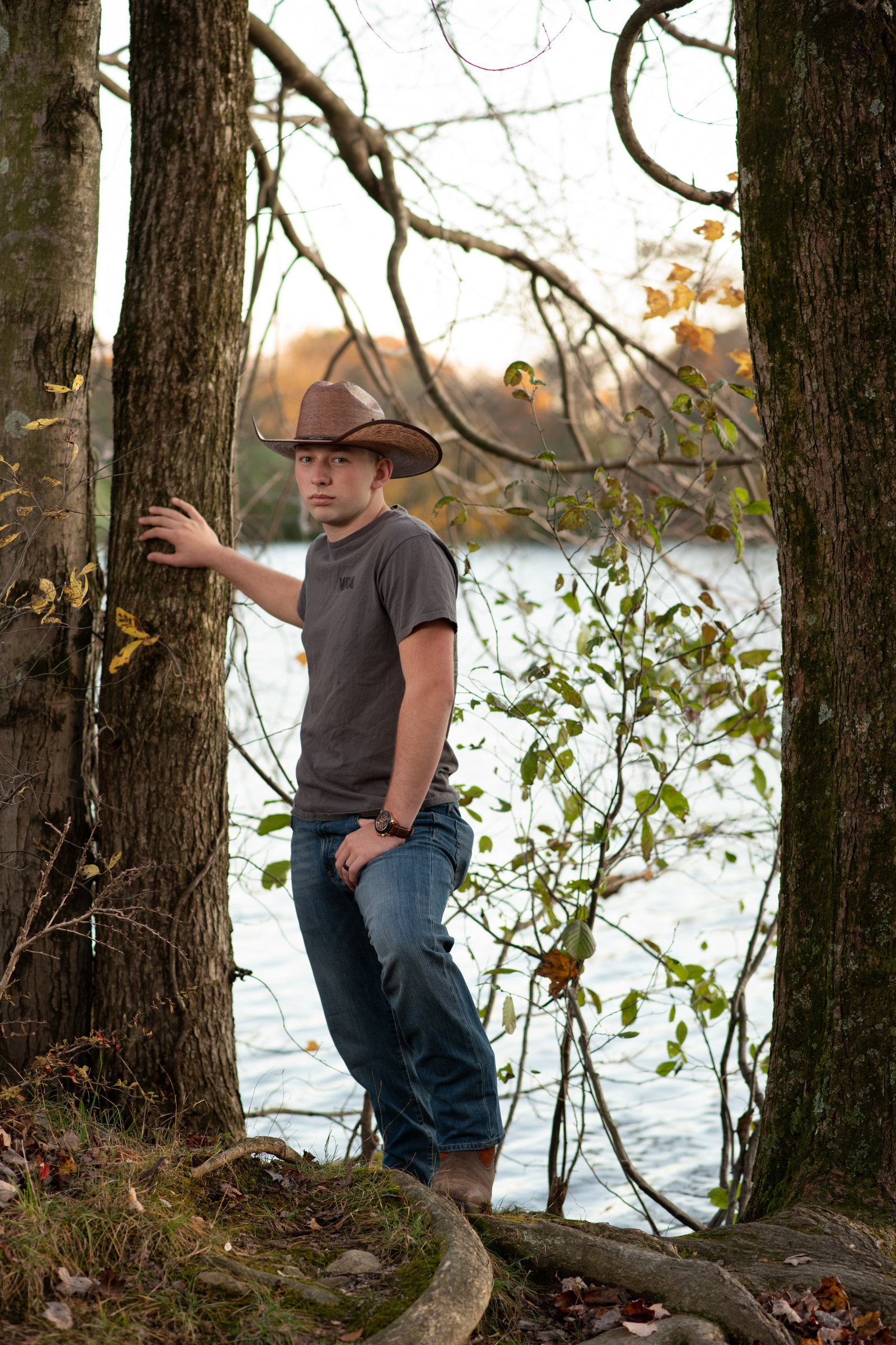 Senior boy in western hat and boots in front of lake