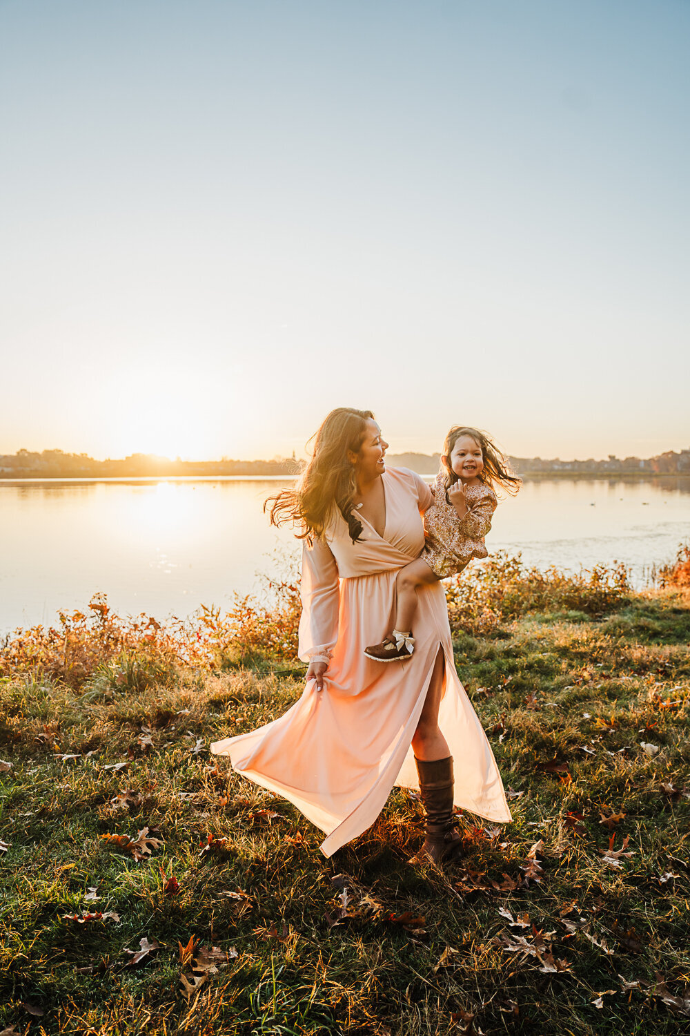 mom twirls dress holding a toddler girl at sunrise