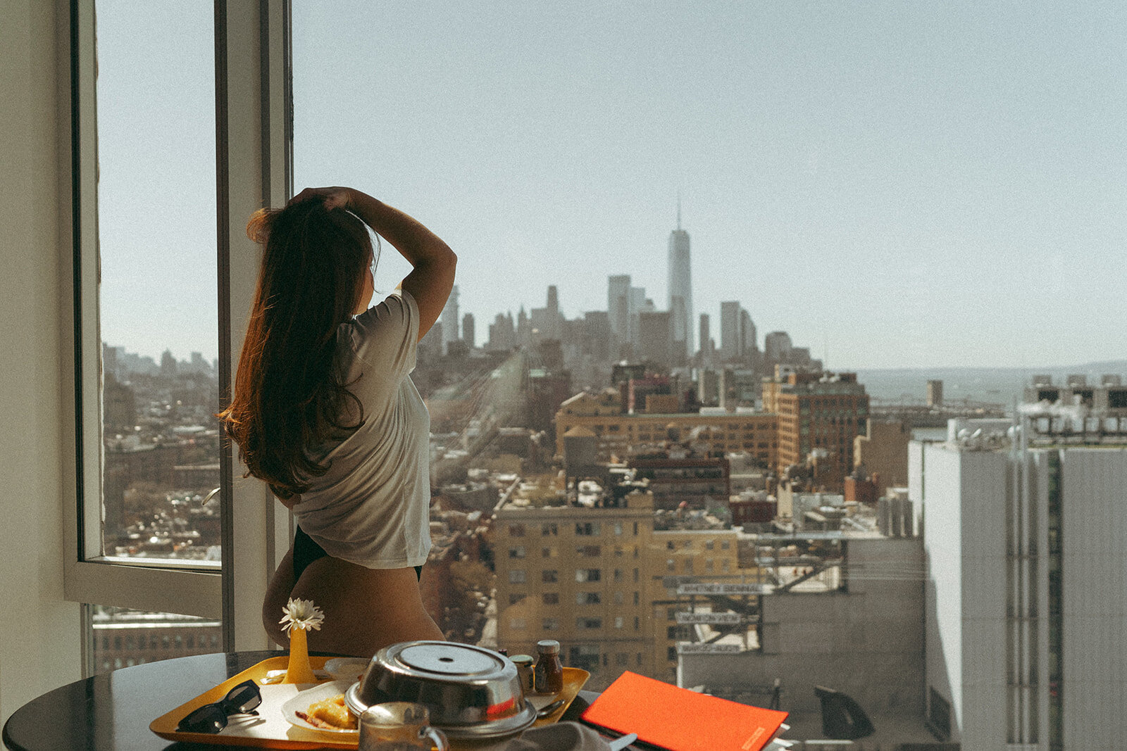Woman looks at skyline while taking boudoir photos in NYC hotel by Elsie Goodman.