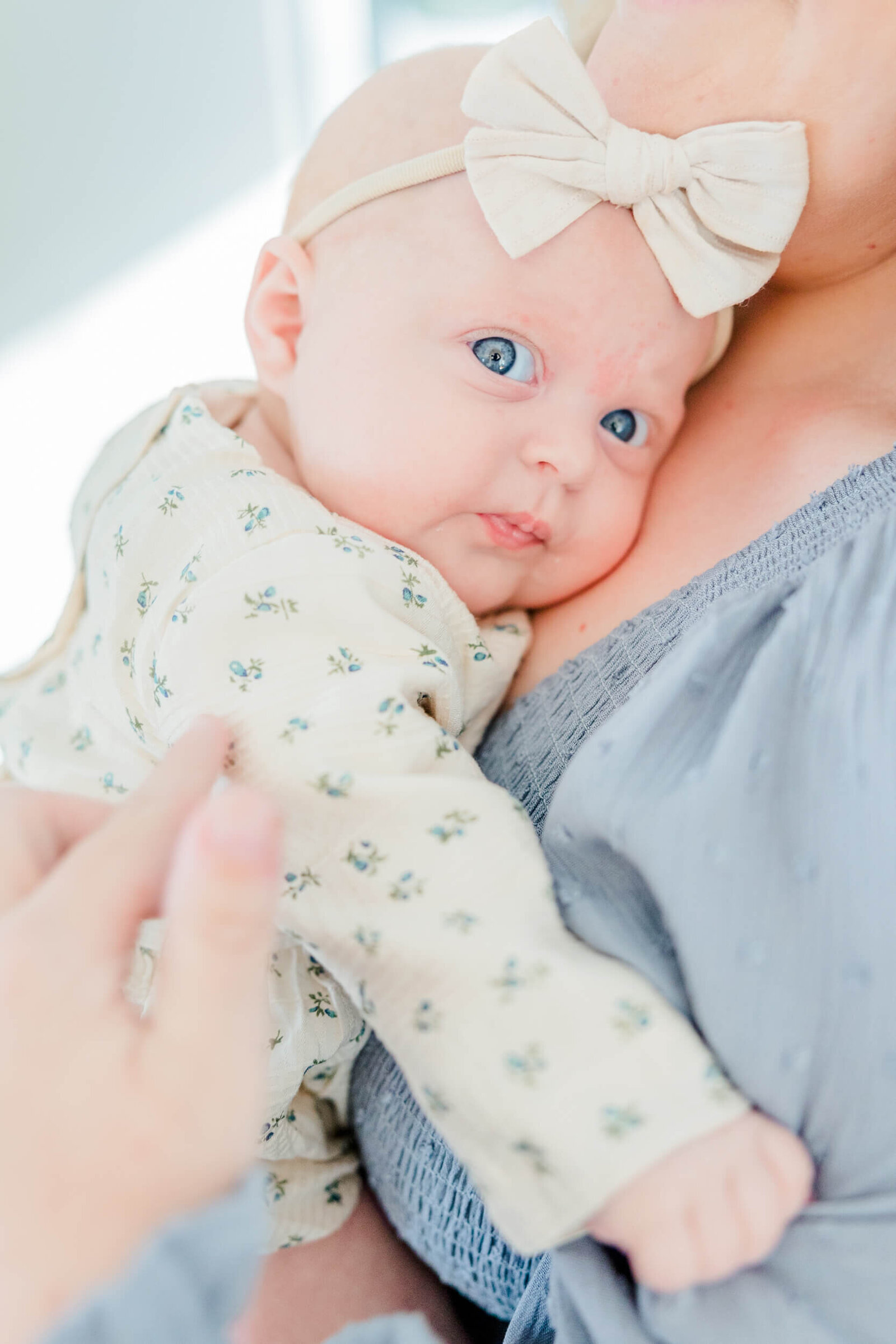 Baby with a bow leans into  her mom's chest and looks cautiously toward the viewer