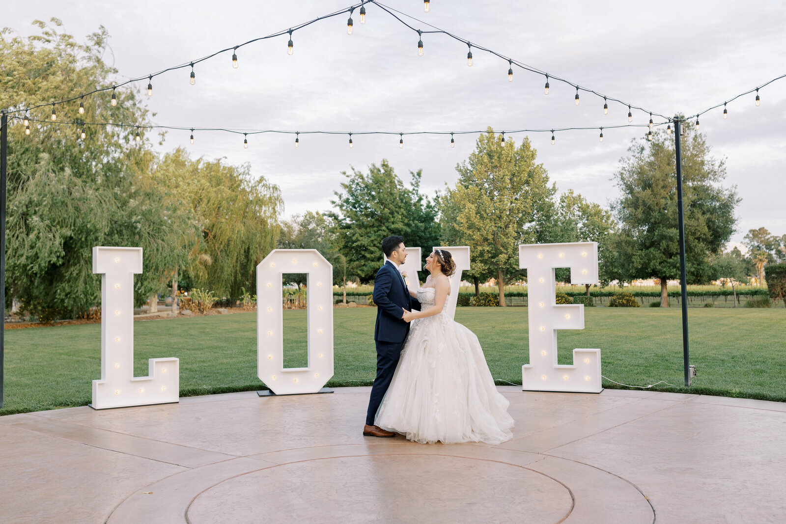 sacramento wedding photographer photographs bride and groom dancing outside in front of large white letters that spell out LOVE with a green lawn behind it and string lights above them