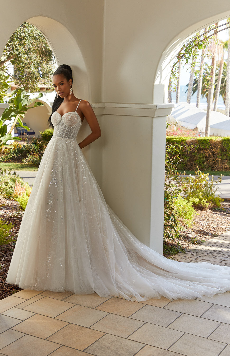 Bride in a sparkly A-line wedding gown with thin straps standing under an outdoor archway