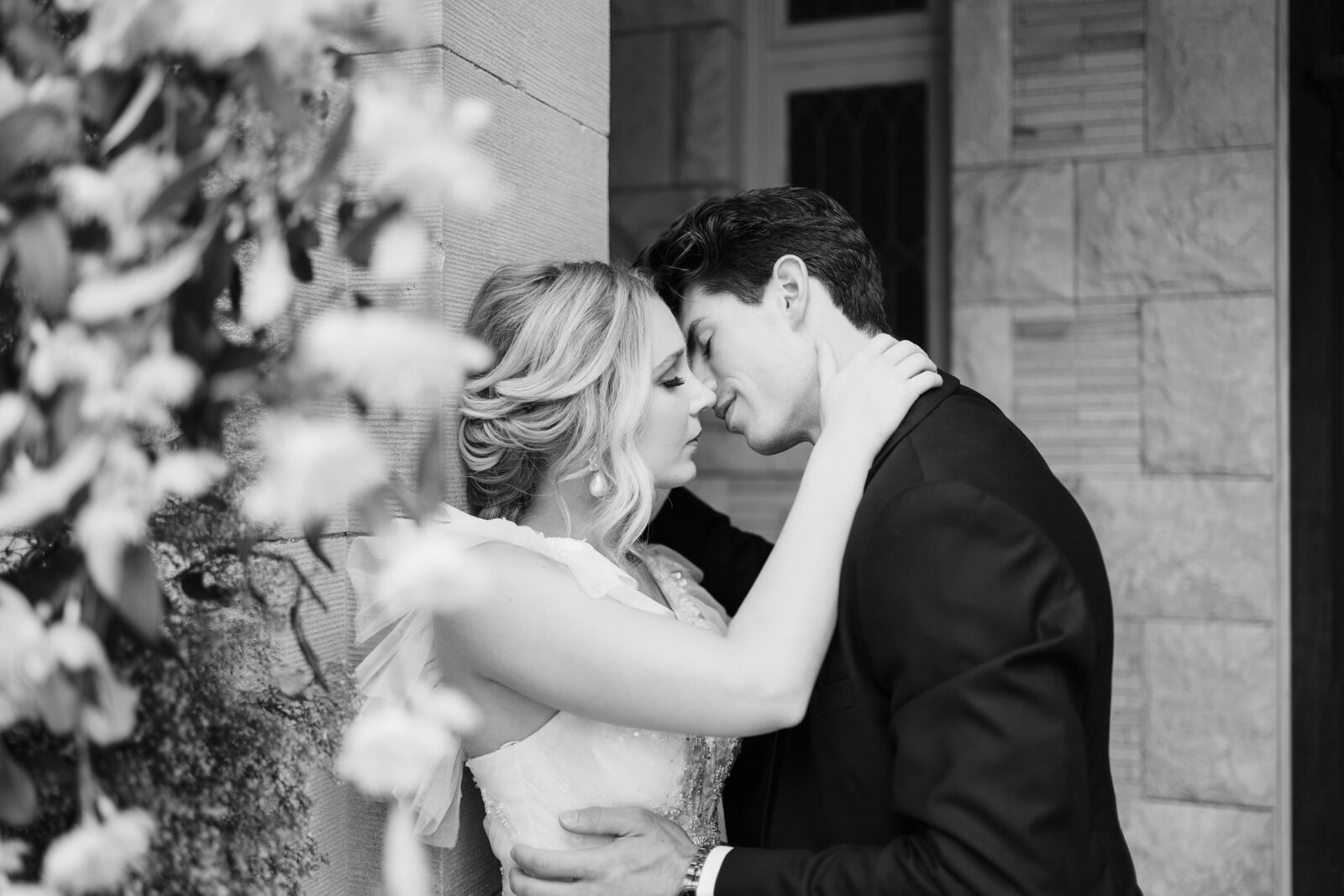 A bride leans against the wall of a villa while her husband leans in for a kiss