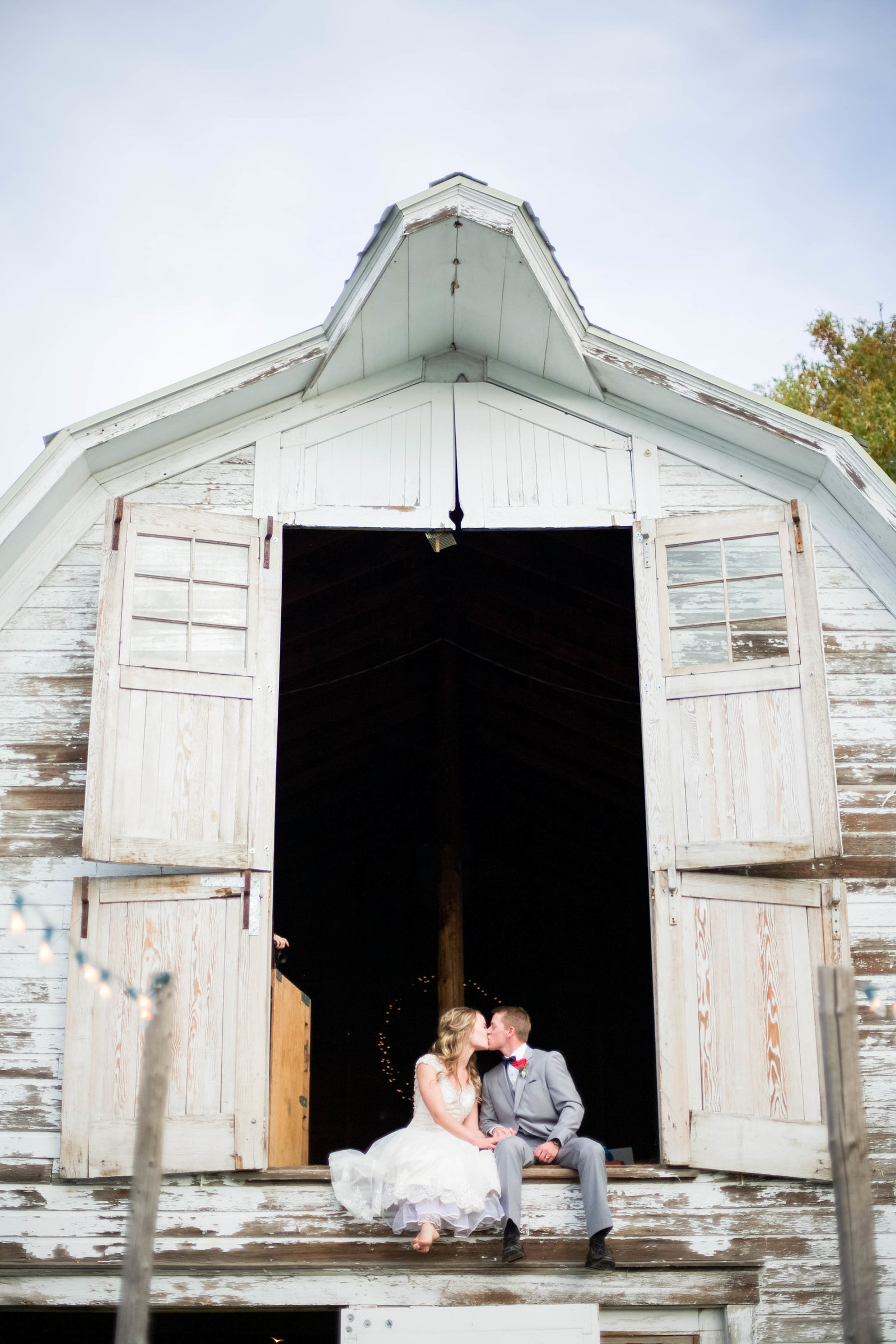 A man and woman kissing in front of a barn on their wedding day.