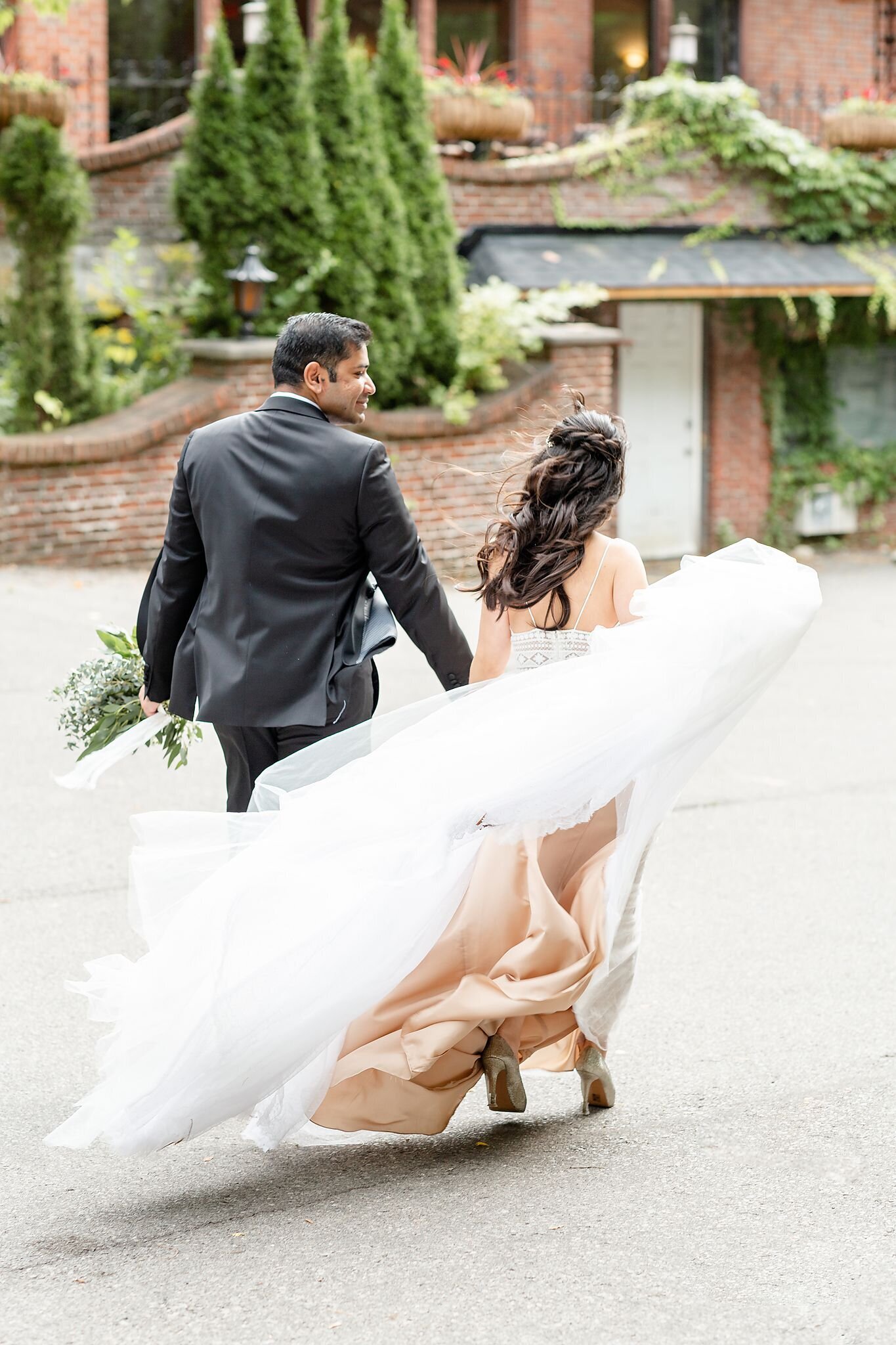 Bride-and-groom-walking-around-their-wedding-venue-with-the-wind-blowing-through-the-dress