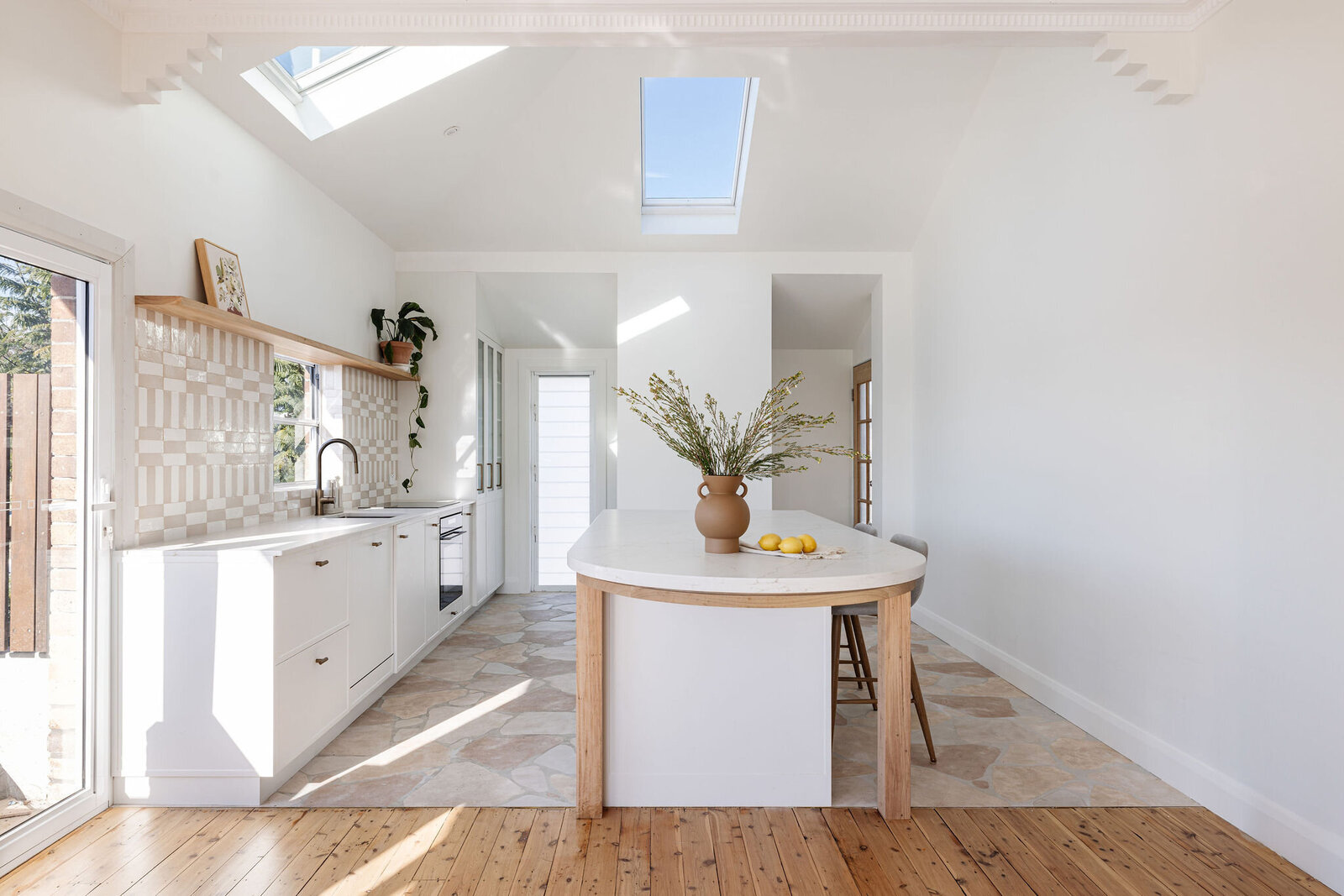 Bright kitchen designed by a luxury home design expert in Newcastle, featuring skylights, white cabinets, an island adorned with flowers and lemons, and elegant wooden flooring.