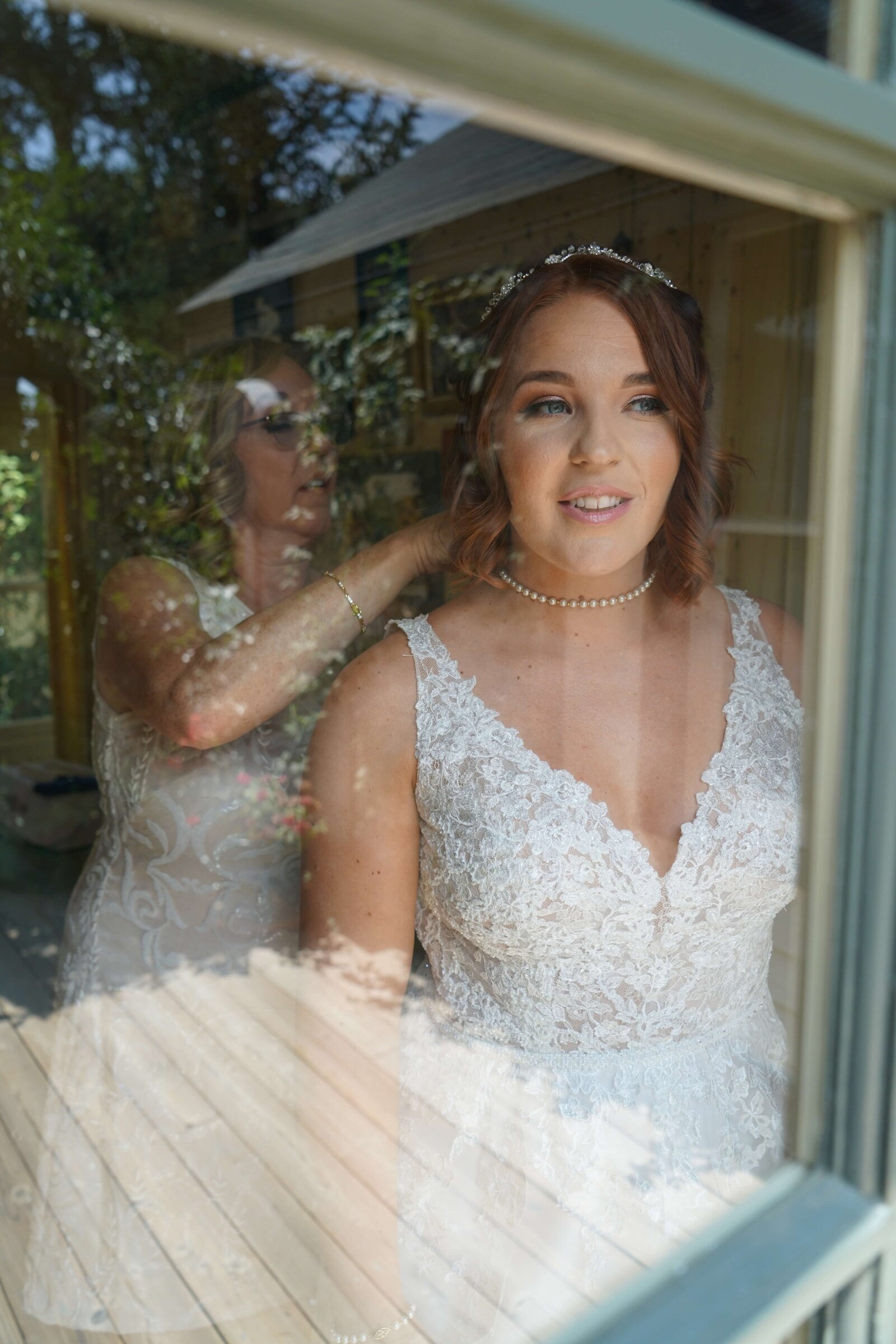 Newport Beach Wedding Photographer portrait of bride looking out window while the mother of the bride puts on her necklace