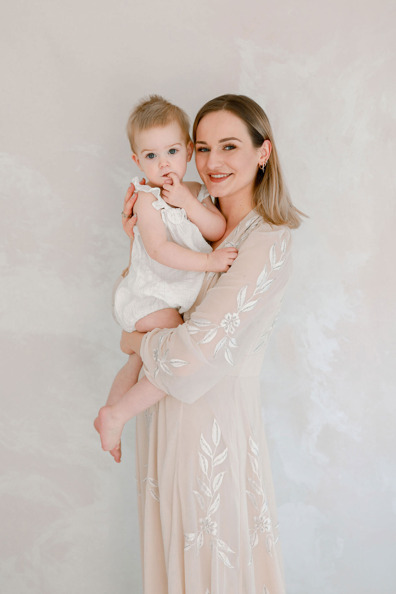 Mama in einem cremefarbenem eleganten Kleid mit ihrem süßen Baby auf dem Arm bei einem Babyfotoshooting in Bielefeld nahe Verl, Paderborn und Gütersloh.