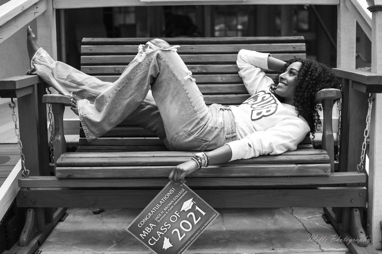 black and white photo of a high school senior laying on a bench showing off her college acceptance letter photographed by Millz Photography in Greenville, SC