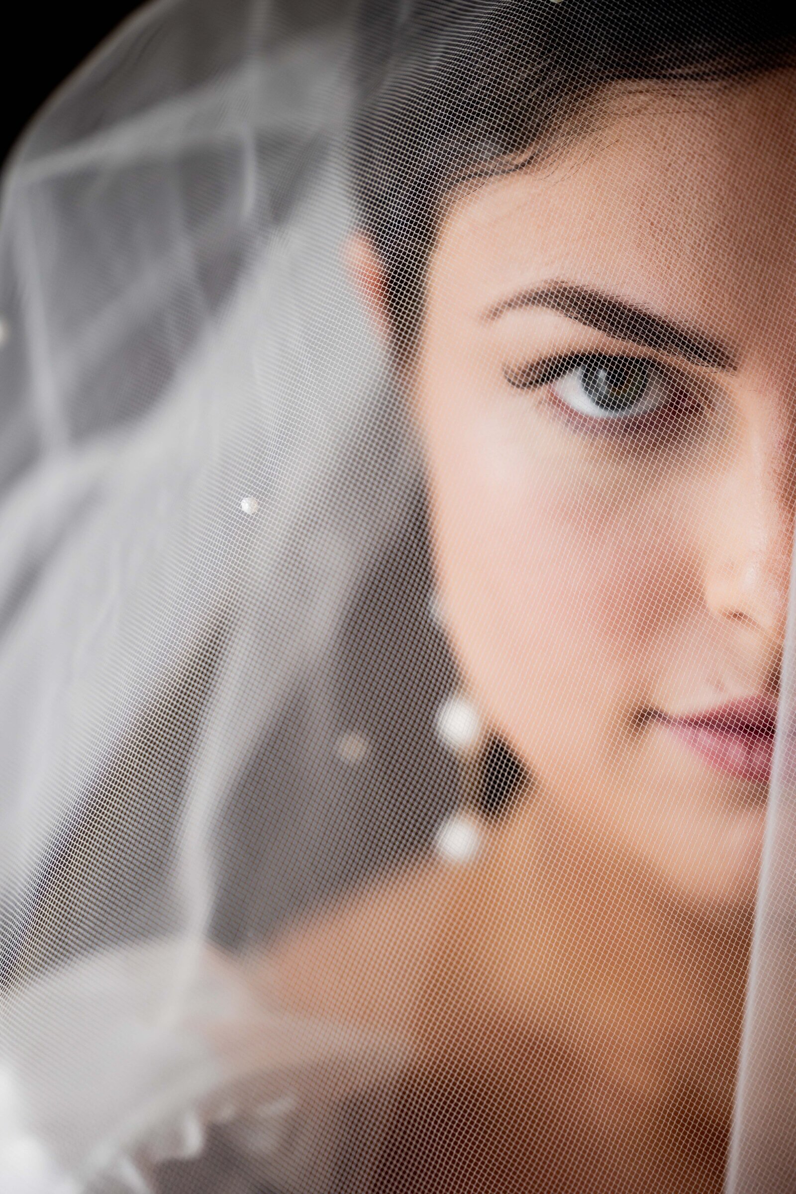 Step into the ethereal elegance of Katherine’s wedding day with this stunning portrait captured under her delicate veil. This image beautifully highlights the intricate lace details of the veil as it softly envelops her, creating a serene and intimate atmosphere. The photograph emphasizes Katherine's grace and the exquisite features of her bridal look, making it a captivating inspiration for brides who envision a classic and romantic wedding style.
