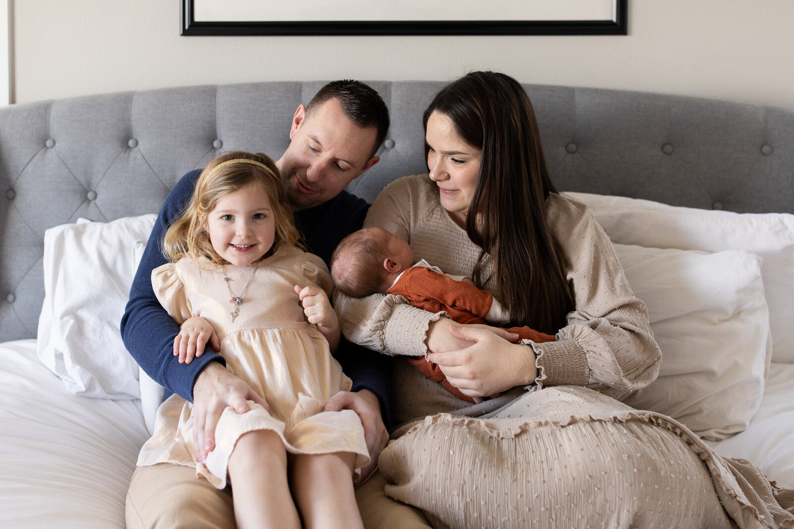 Family sitting on bed hugging with newborn in moms arms.