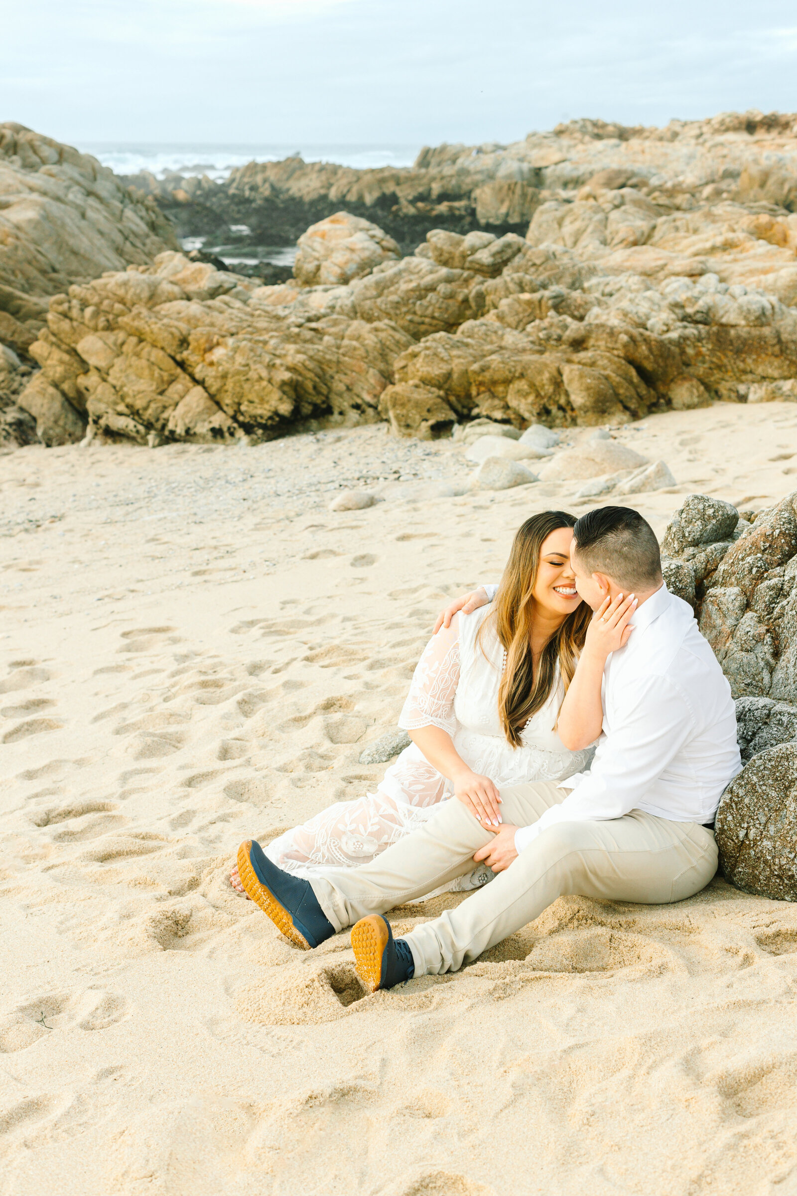 An engaged man and woman take photos on the beach in Pacific Grove, Monterey, California near Big Sur.