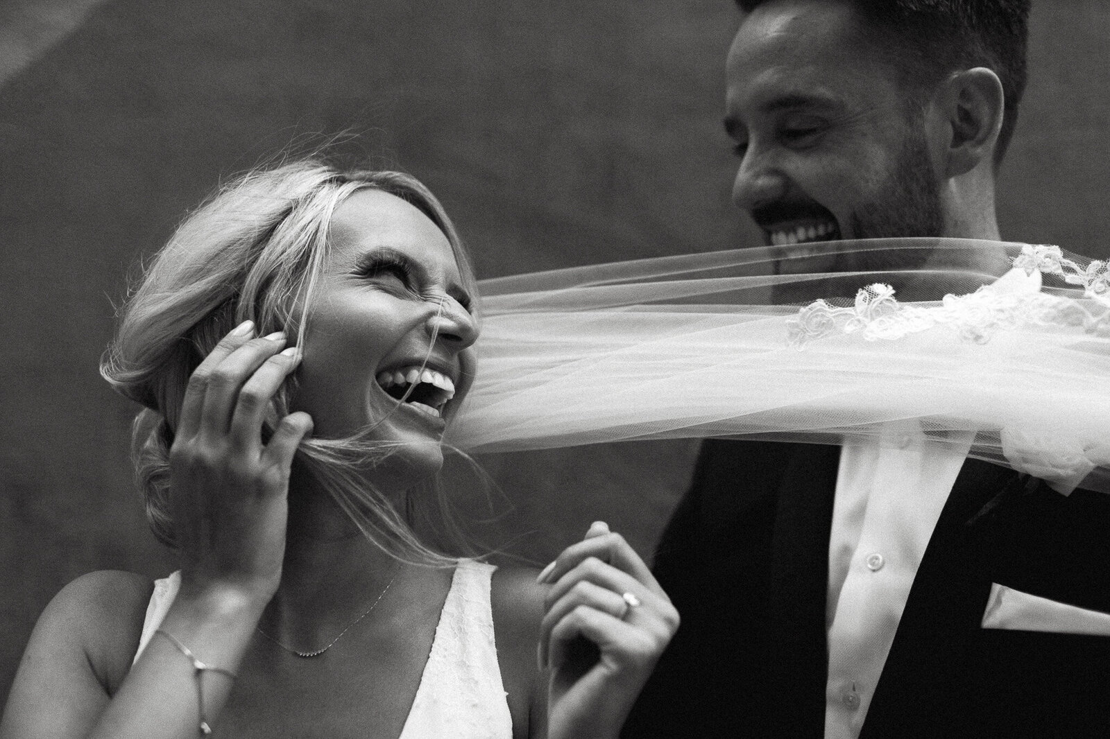 A bride laughing as her veil playfully drapes over a smiling groom, captured beautifully by a Toronto wedding photographer in downtown Toronto.