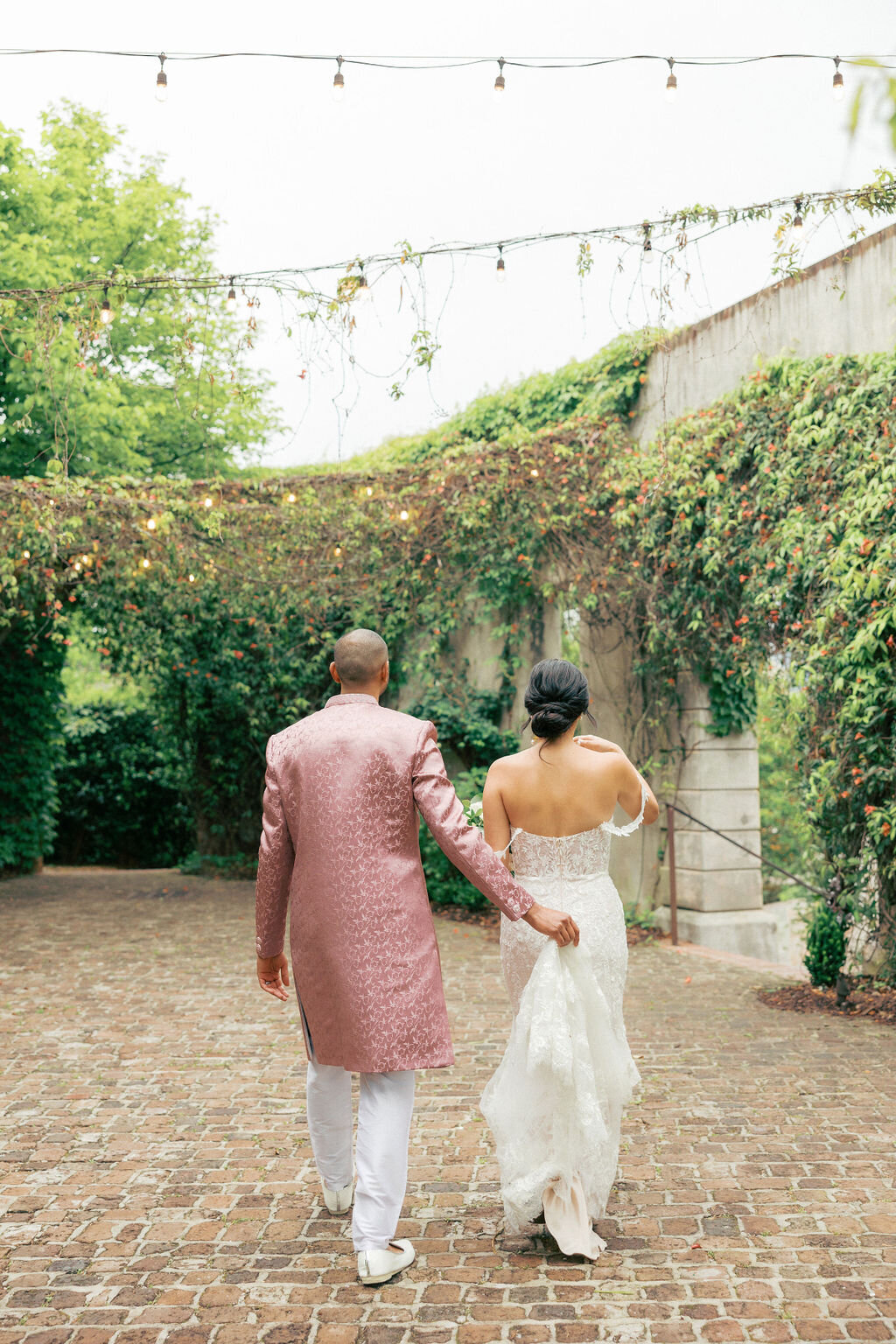 Groom in Indian dress walks bride through courtyard of Summerour Studio