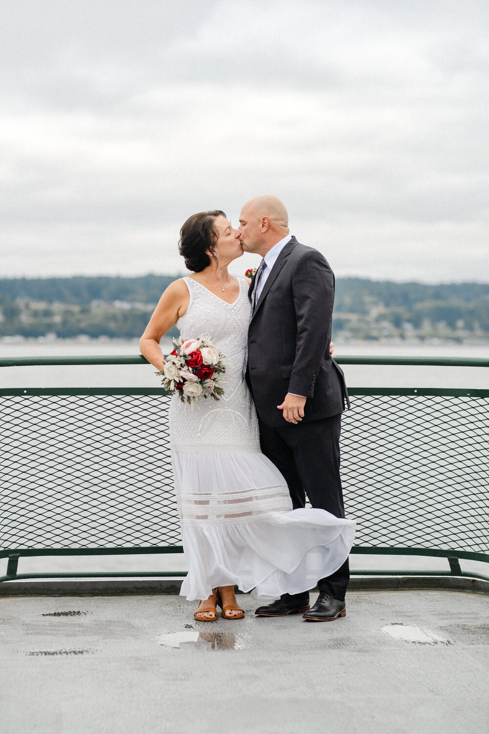 Bride and groom kiss while standing at the front of a ferry
