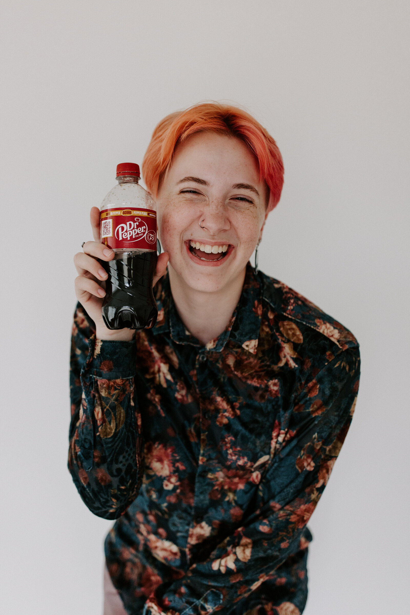 person smiling while holding a bottle of Dr. Pepper up to their face
