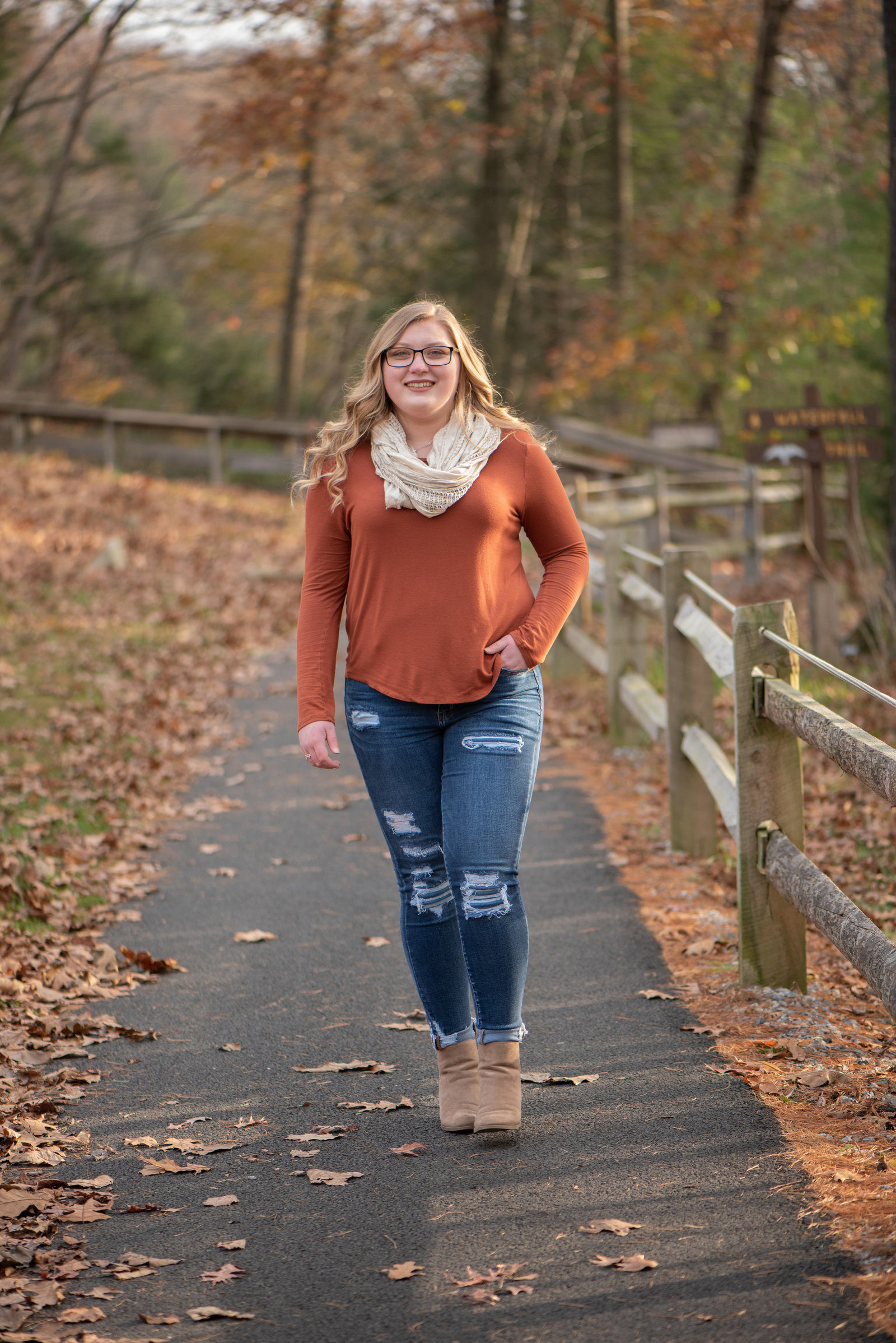 Senior girl in orange top walking on fence-lined path