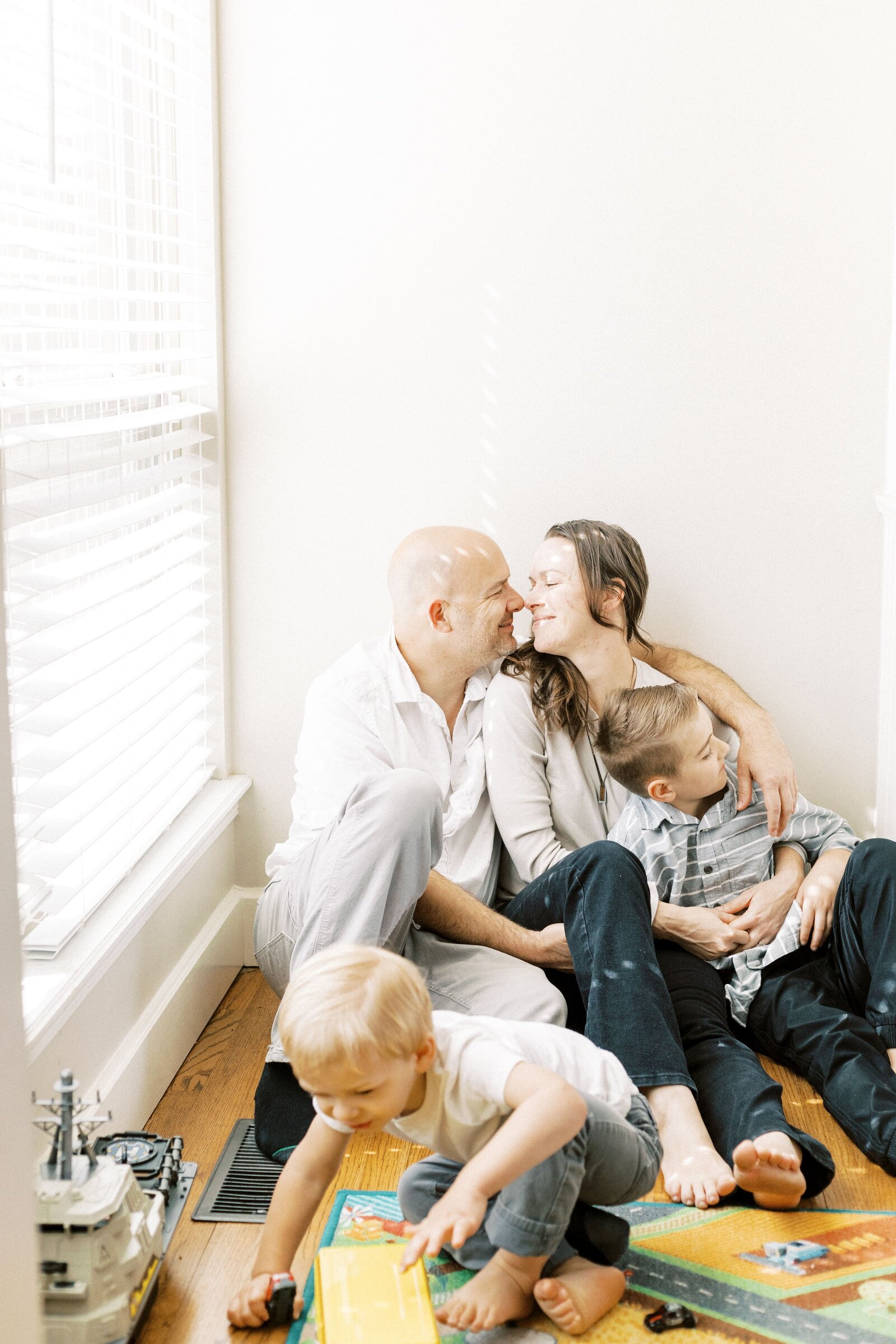 mom and dad sitting in corner of living room while kids play during peoria illinois family photos 