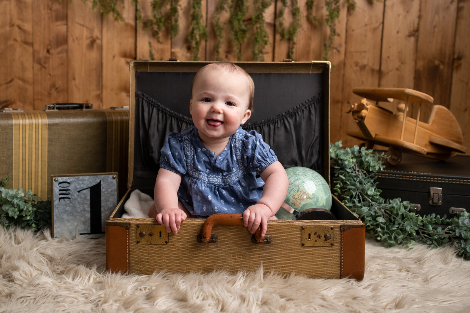Happy baby in a travel themed set sitting in a suitcase