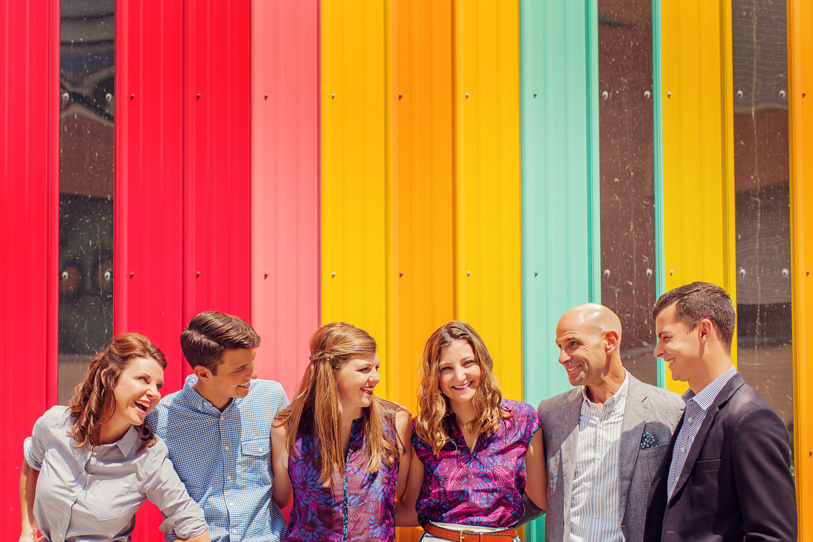 A very colorful shot of a family of six with older kids. A rainbow colored wall is behind them.