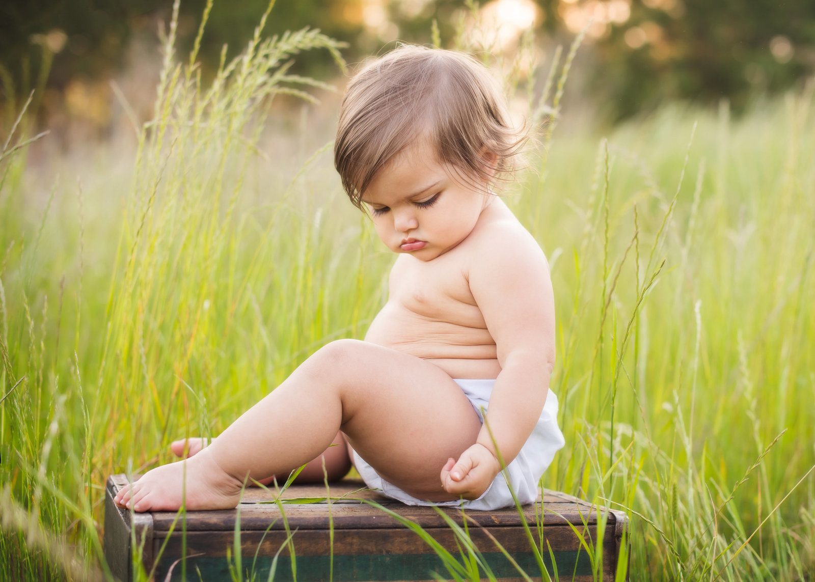 chubby baby sitting on a box  in tall grass
