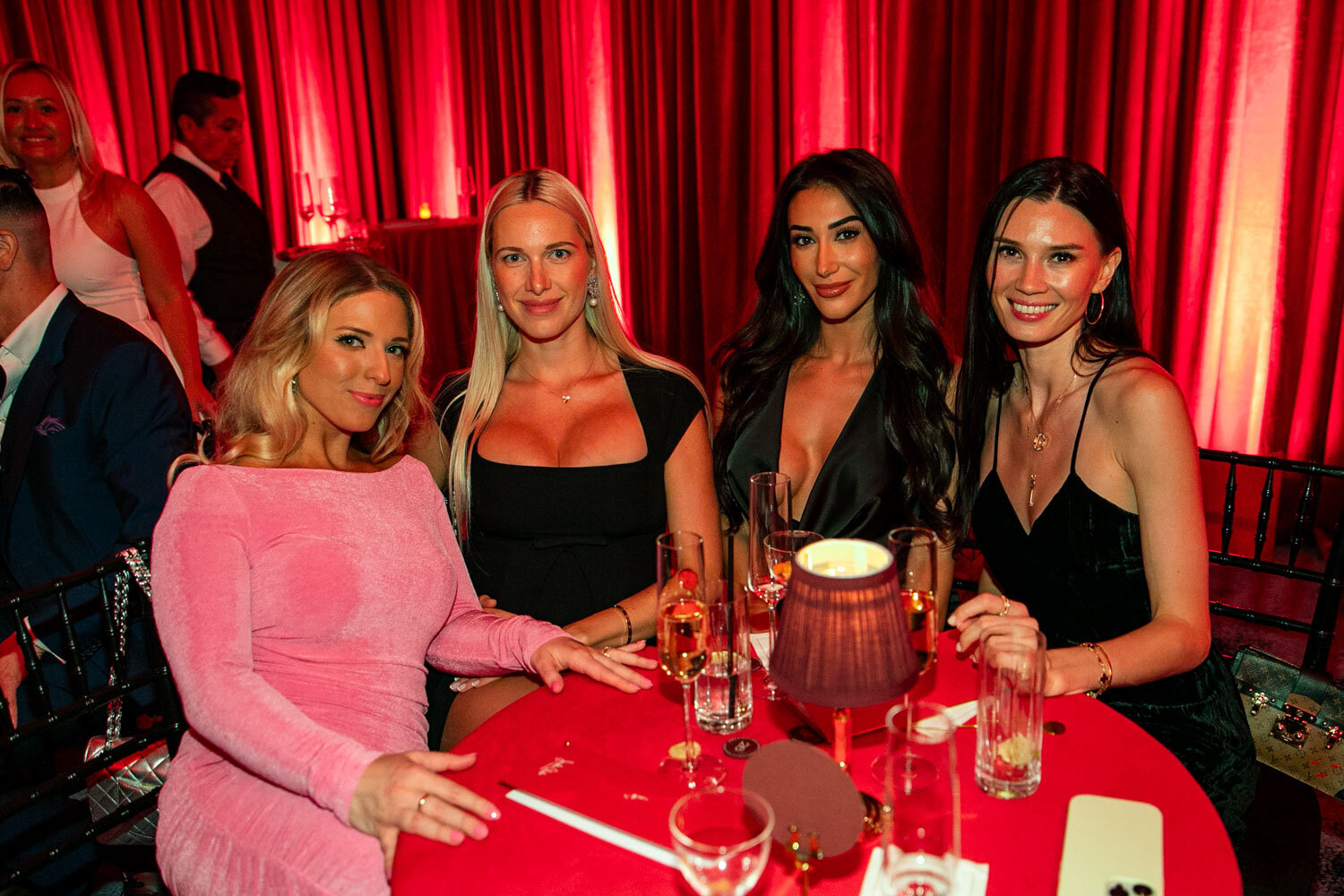 Four women seated at a red table enjoying a glamorous night out