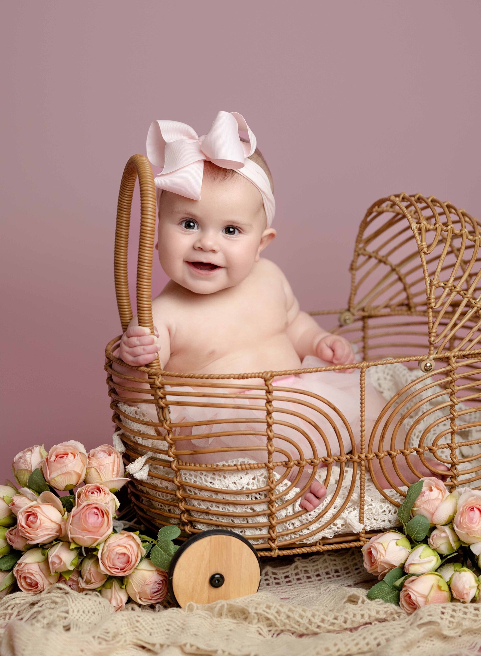Baby girl sitting in bamboo carriage and smiling with roses by the carriage.
