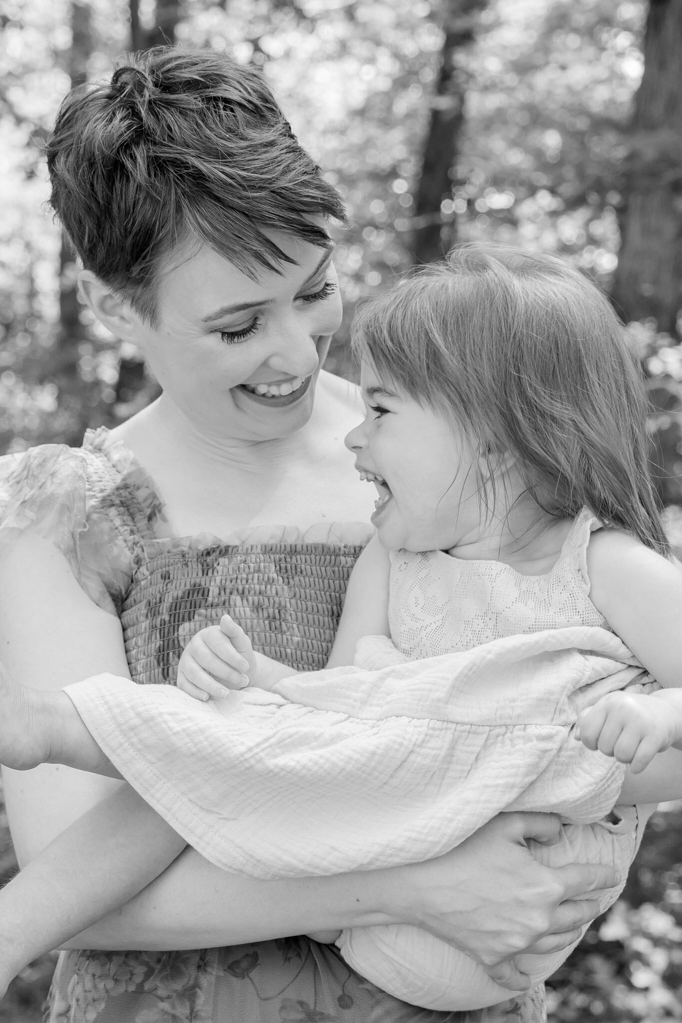 Black and white photo of mom holding her baby girl, both laughing and smiling at each other.