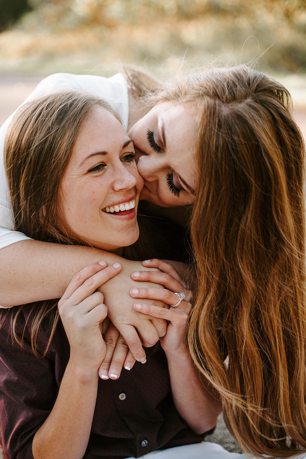 Couple cuddling together with girl kissing her girlfriend on the cheek from behind during their Minneapolis engagement session