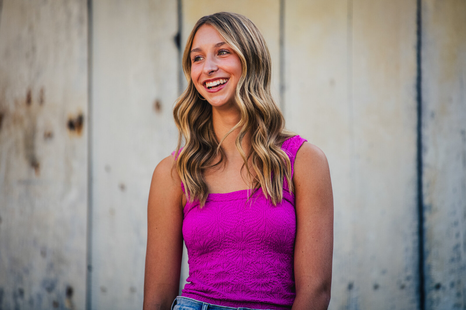 a high school student stands in front of a barn during her photo shoot