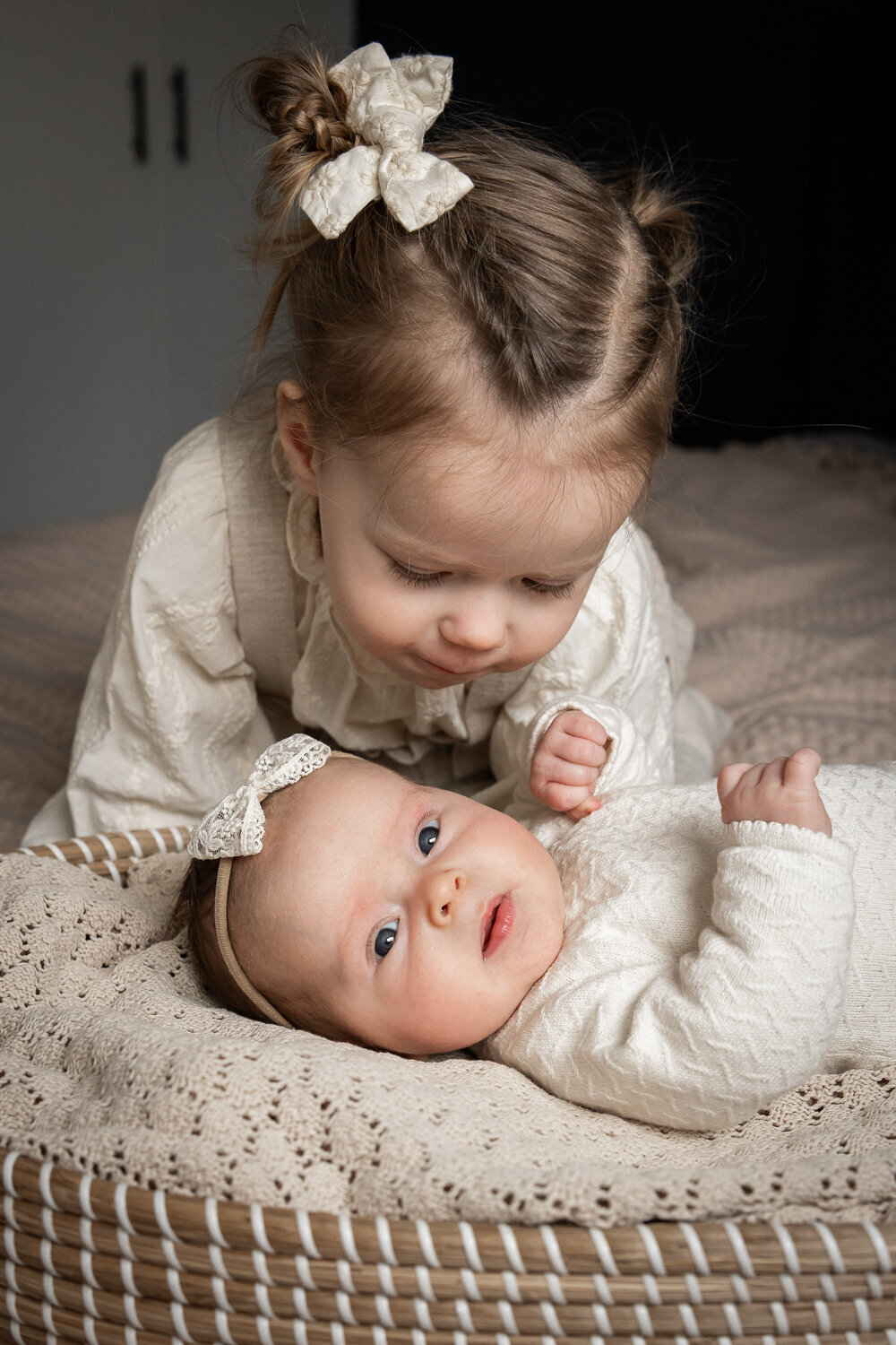grote zus kijkt bij haar babyzusje tijdens een fotoshoot op bed, ontspannen bij hen thuis.
