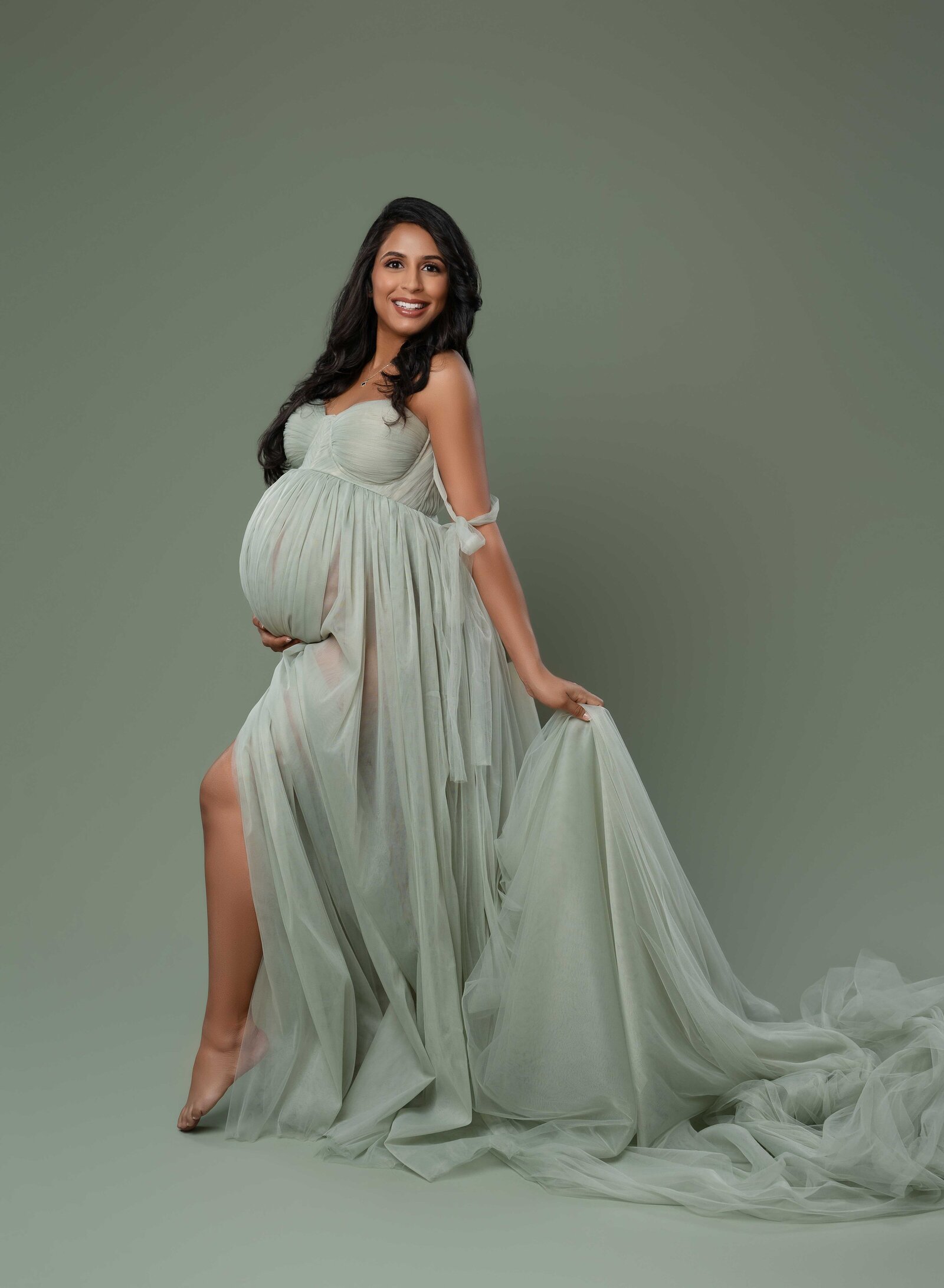 Pregnant women holding tulle of mint green gown and smiling at camera. Photo taken at Atlanta Maternity photo studio.