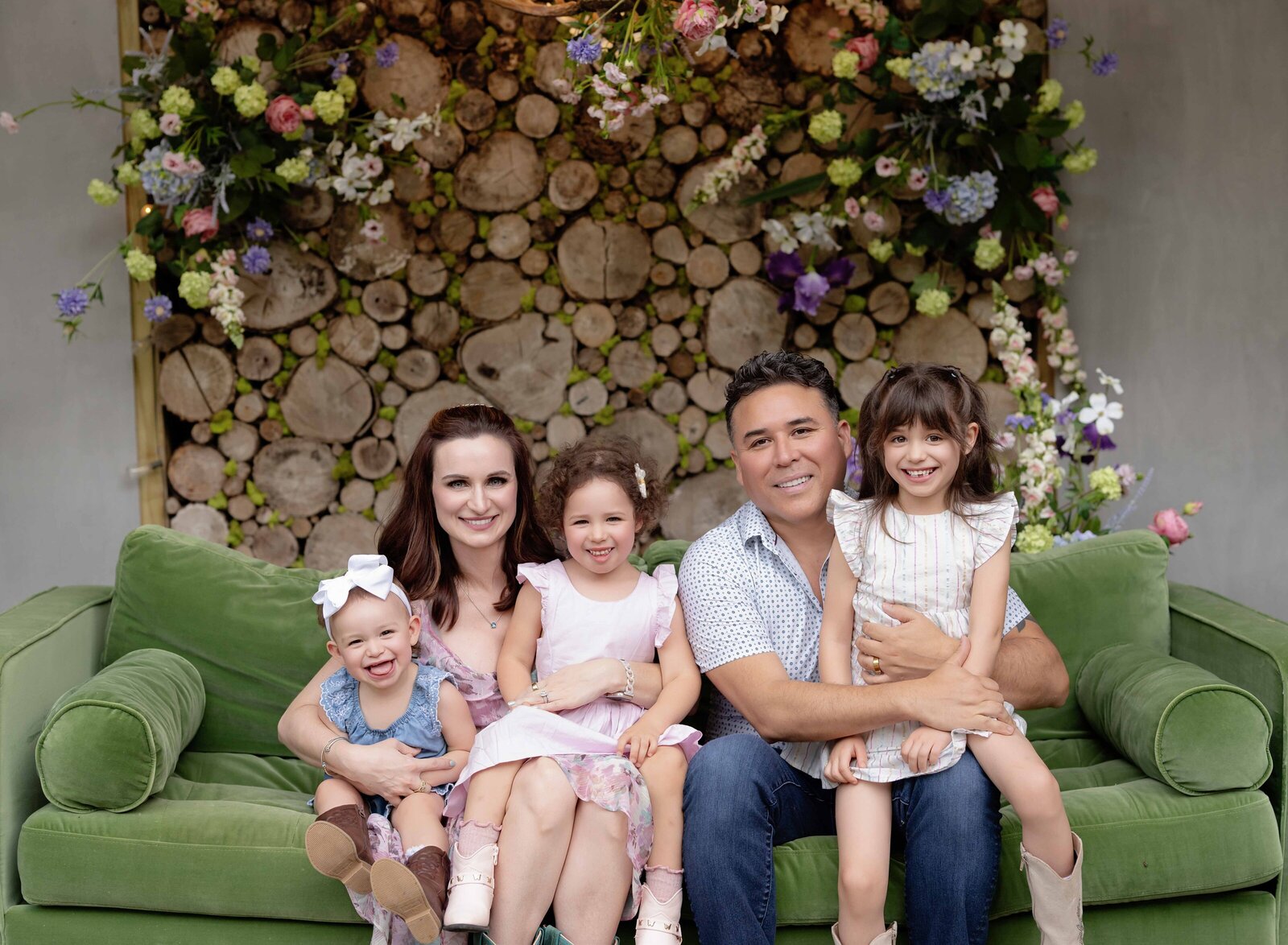 Family of 5 sitting on green sofa smiling and hugging. Photo taken by Jenni Nikki Atlanta Photographer.