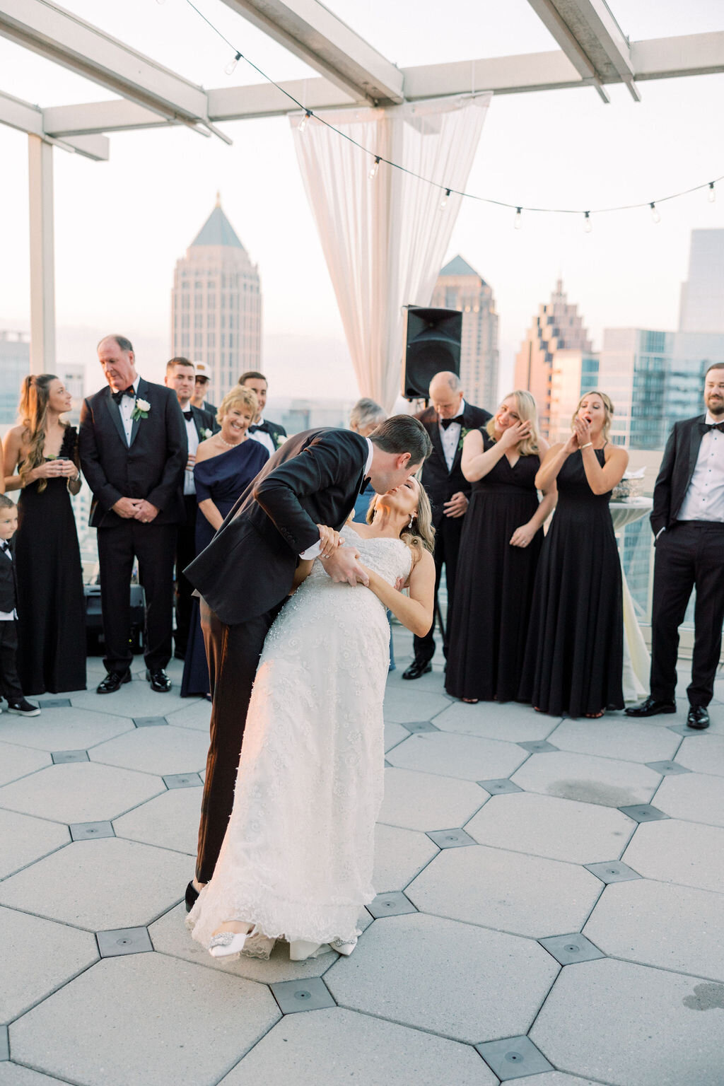 Groom dips bride for a kiss on rooftop with Atlanta Skyline