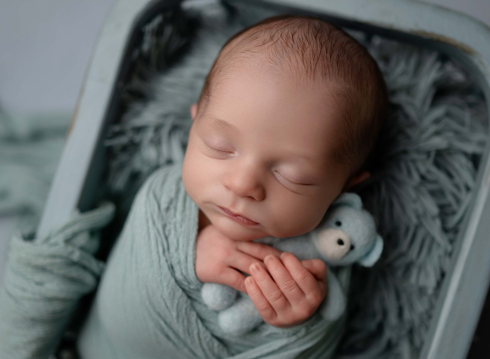 Baby sleeping in crate, holding a blue felted bear. Photo taken by Jenni Nikki at Newborn photo studio in Marietta, GA.