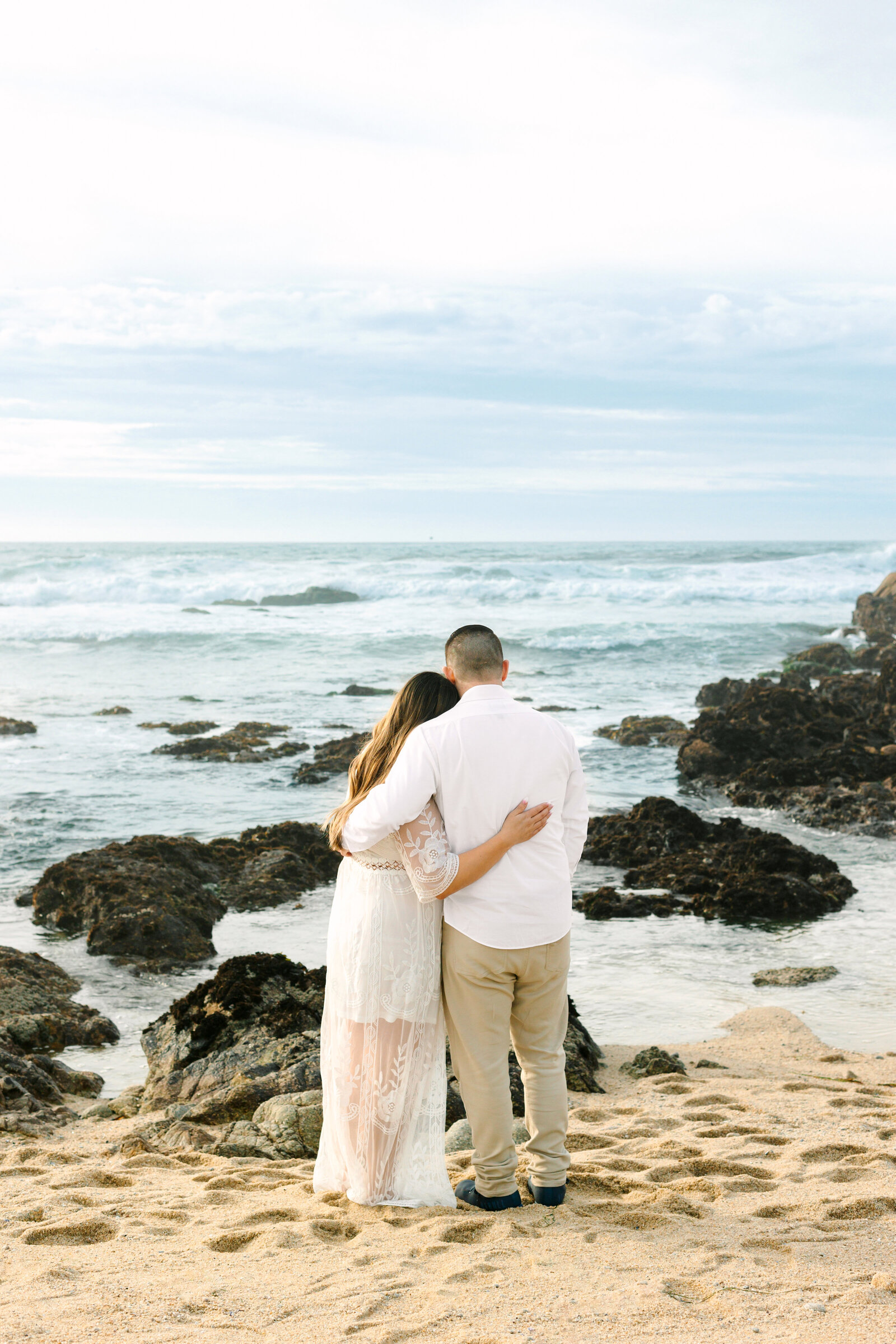 An engaged man and woman take photos on the beach in Pacific Grove, Monterey, California near Big Sur.