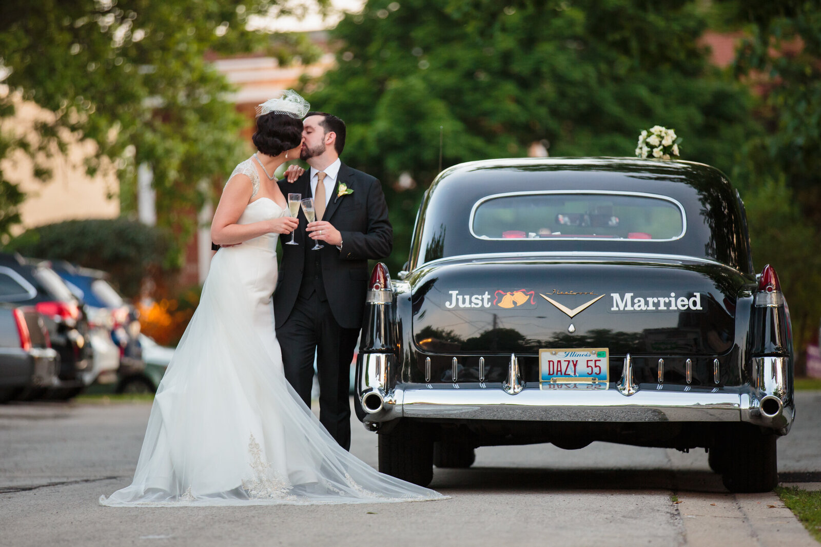 Bride and groom kiss next to vintage car that reads, "Just Married"