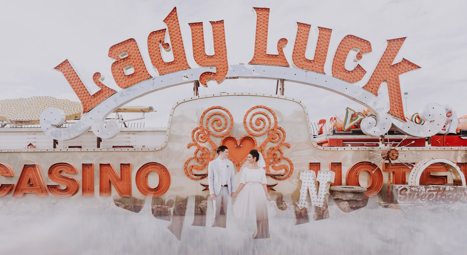 bride and groom pose in front of lady luck sign at neon museum