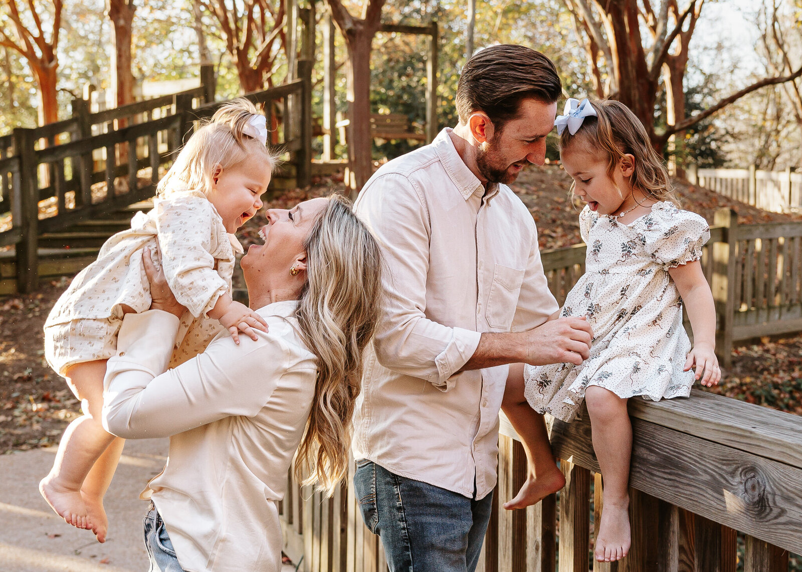 Family session at Hopelands Gardens in Aiken SC - parents smiling with their young children on a wooden bridge under the trees.