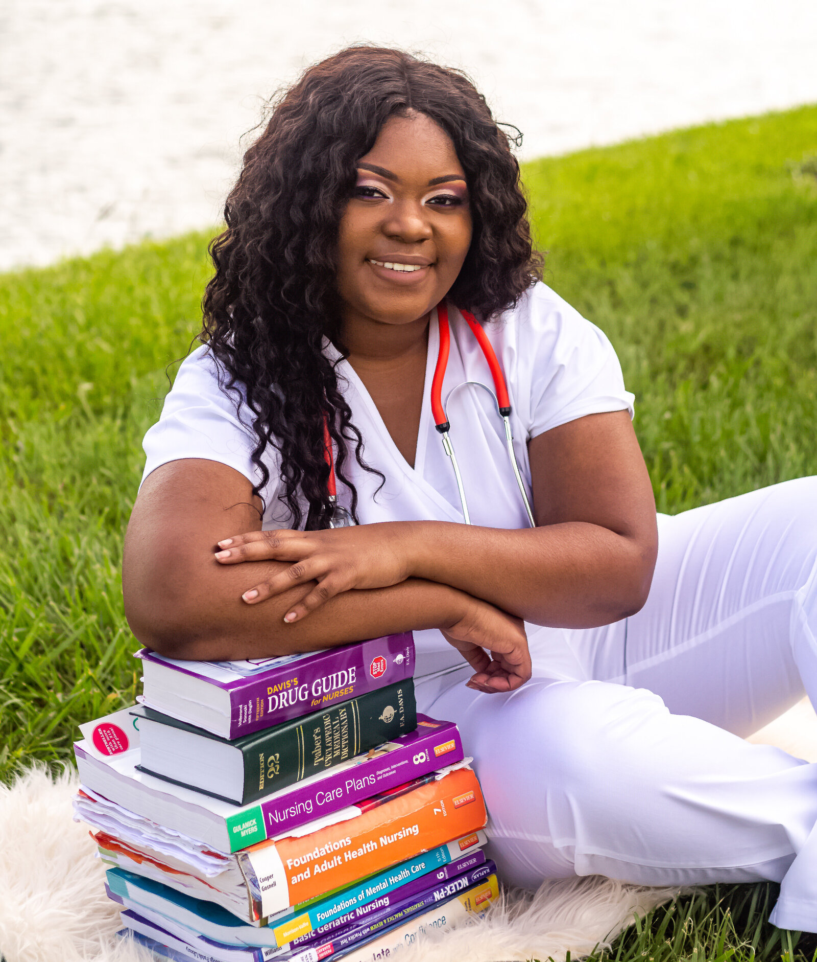 girl in white nursing scrubs sitting on ground leaning on books