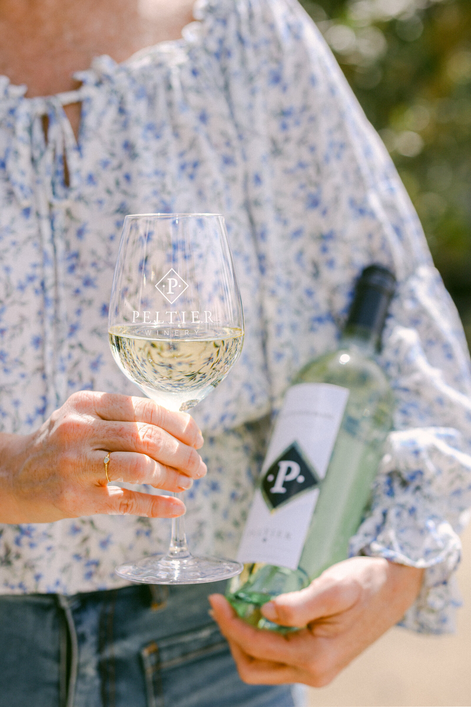woman holding wine bottle and glass of wine in floral print shirt