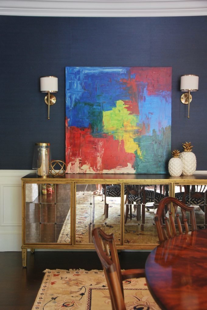 A gold and mirrored buffet and colorful abstract painting on a navy wall.