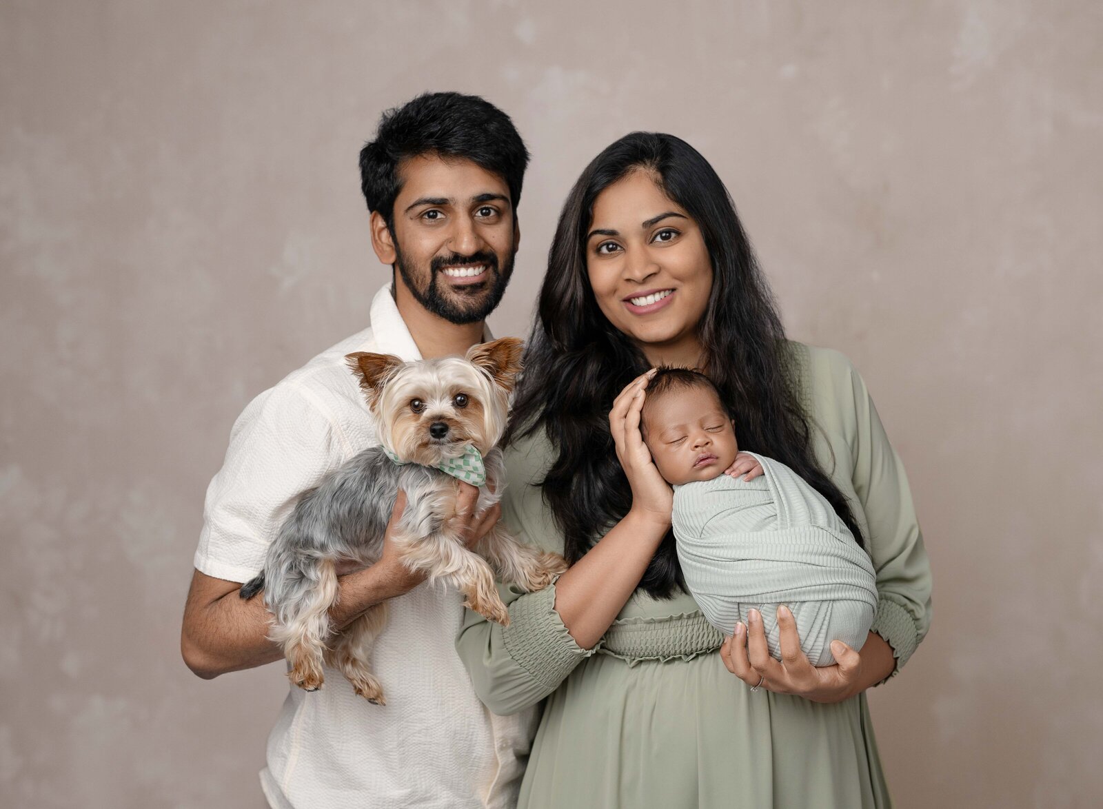 Dad is holding dog and Mom is holding newborn baby, looking at camera. Newborn Photography session photographed at Jenni Nikki's photo studio in Marietta, GA.