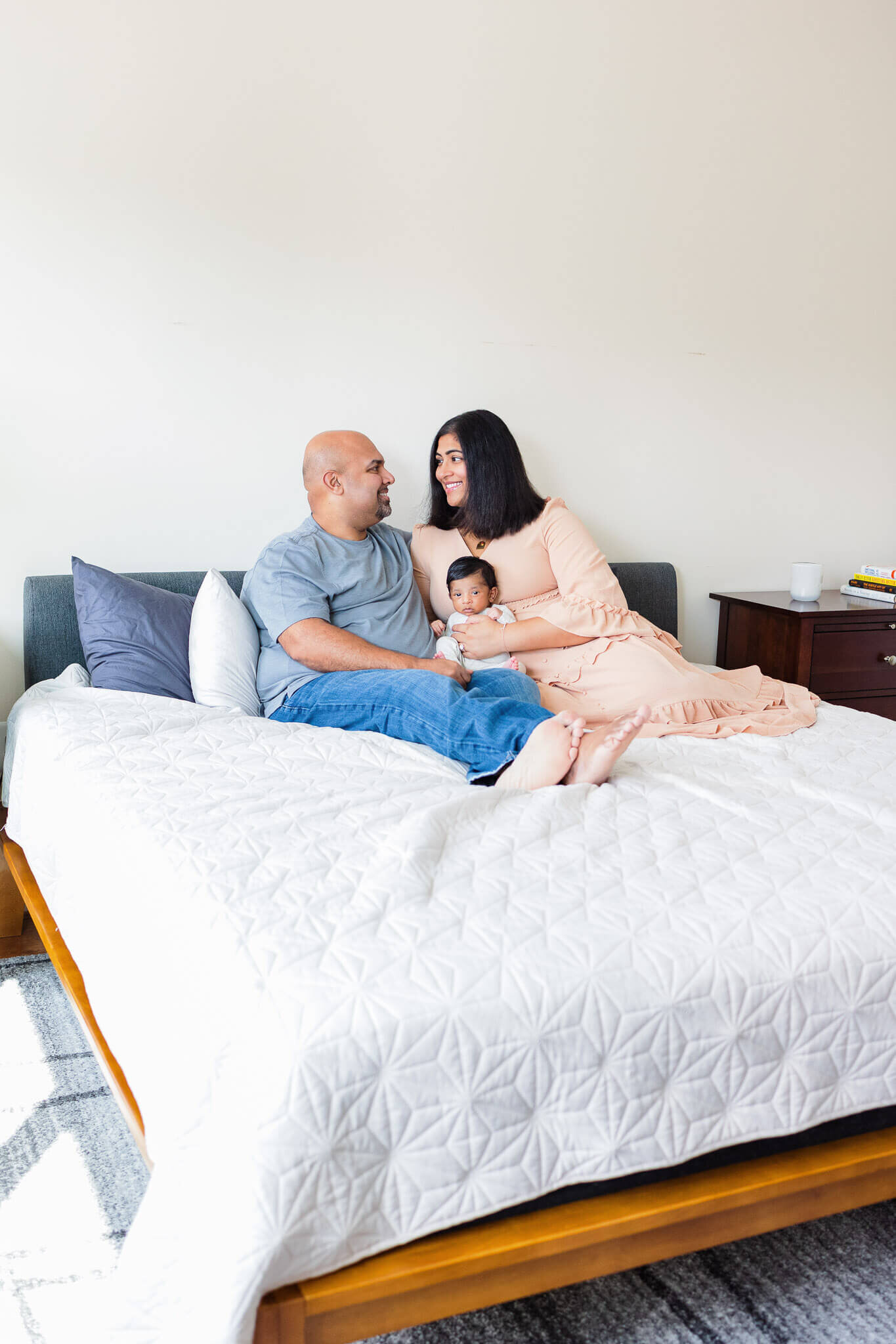 A newborn boy sitting in his parents laps in bed.