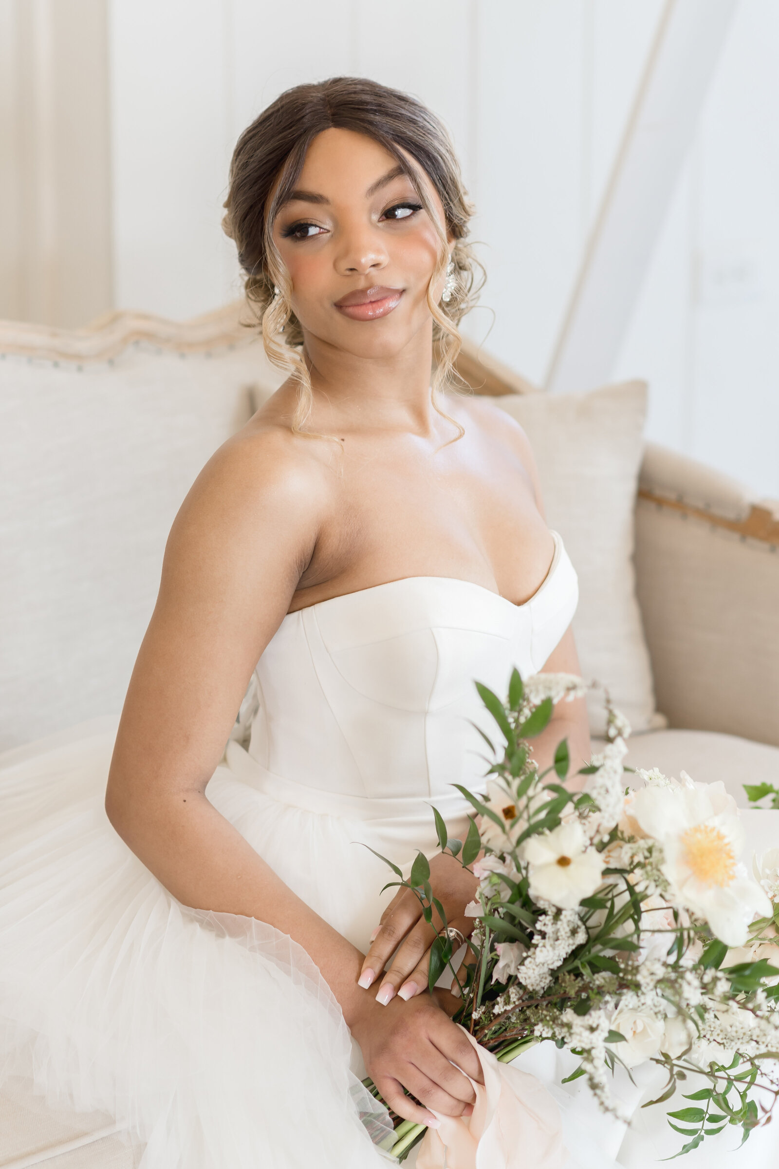 bride sitting on a couch looking slightly over her shoulder while holding her bouquet in her lap