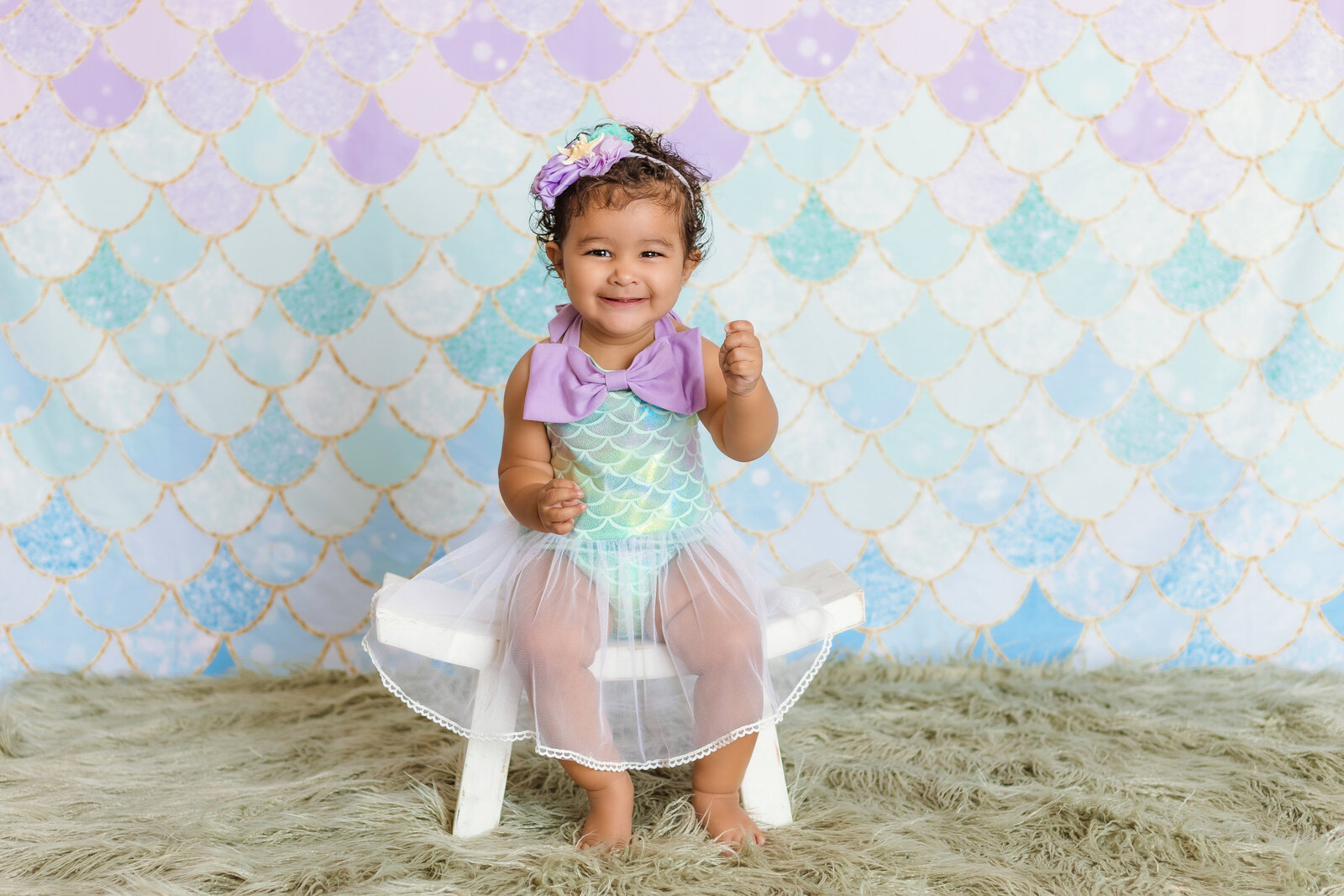Milestone Photographer a baby wears a mermaid costume and sits before a matching scaled wall