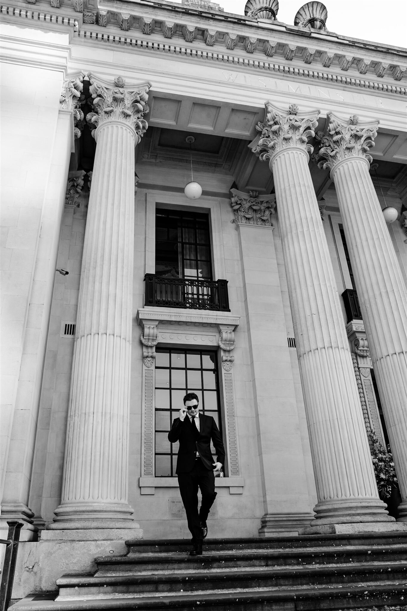stylish groom with sunglasses walking down old marylebone town hall steps. cinematic wedding photography