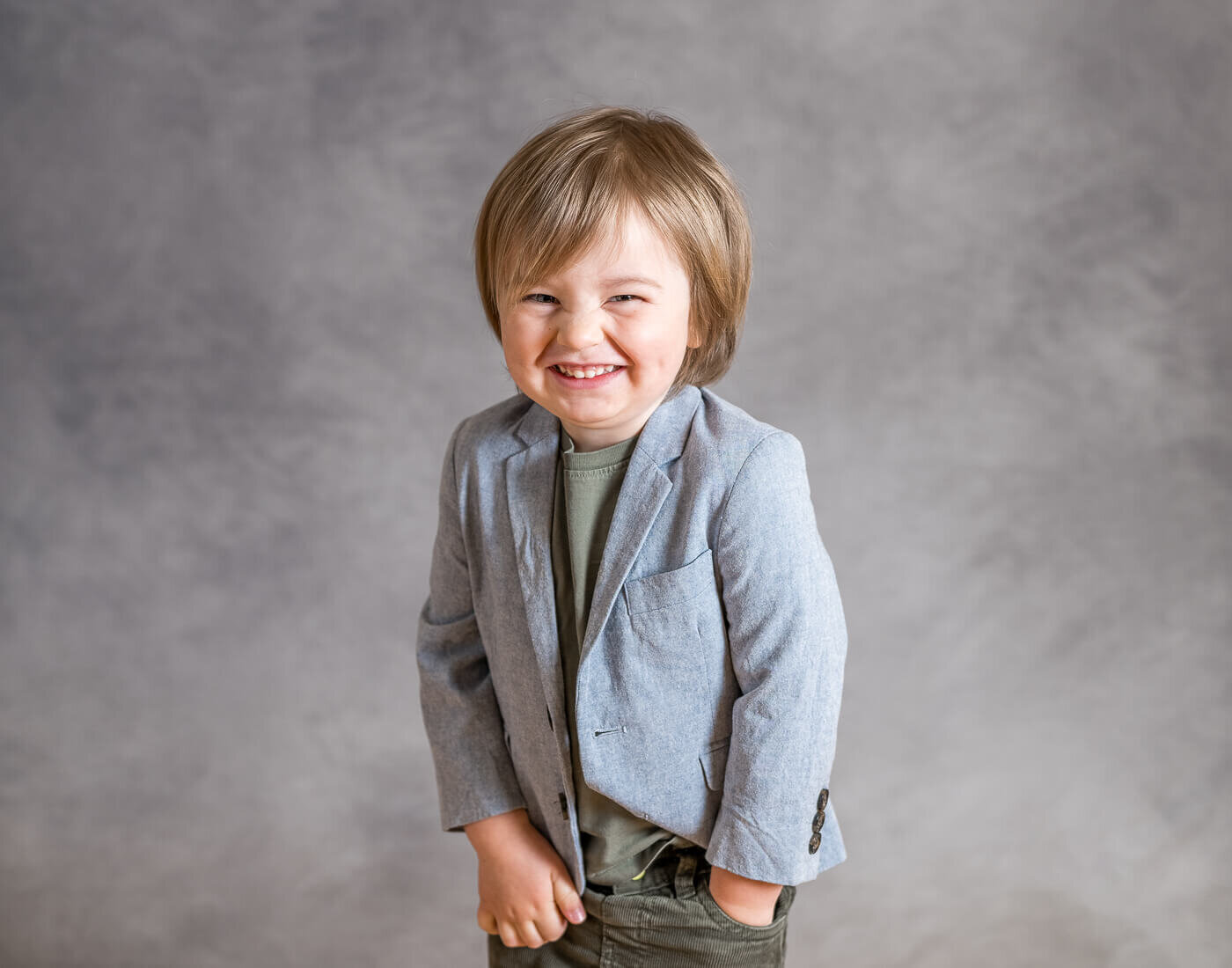A child smiles brightly with their hand in their pocket.