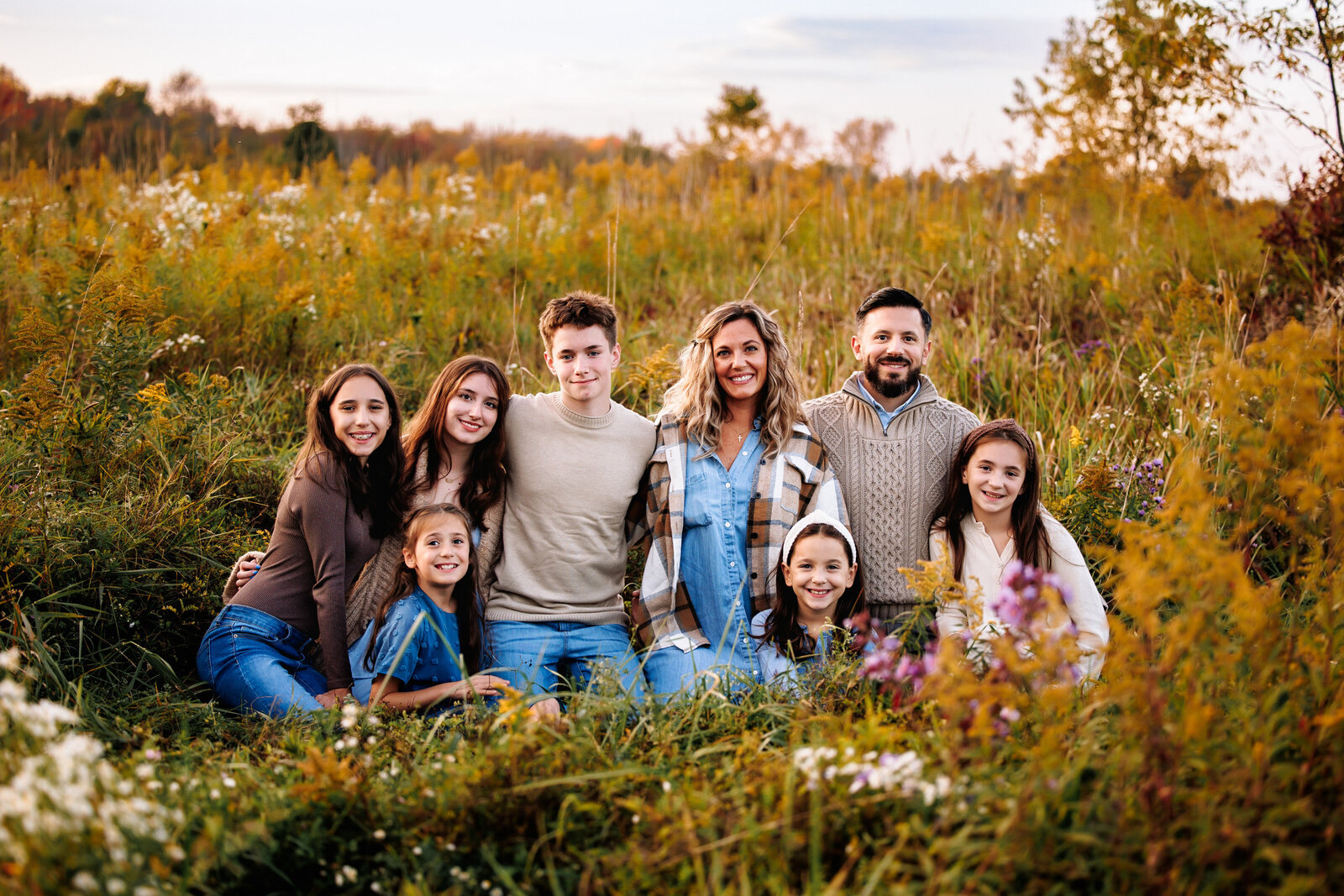 Large family of 8 sit together in a field of tall grasses for a photo