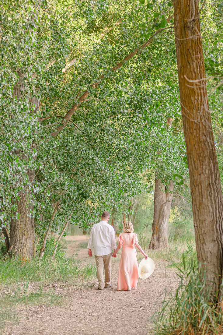 An engaged couple hold hands as they walk along the Jordan River Trail in Murray Utah
